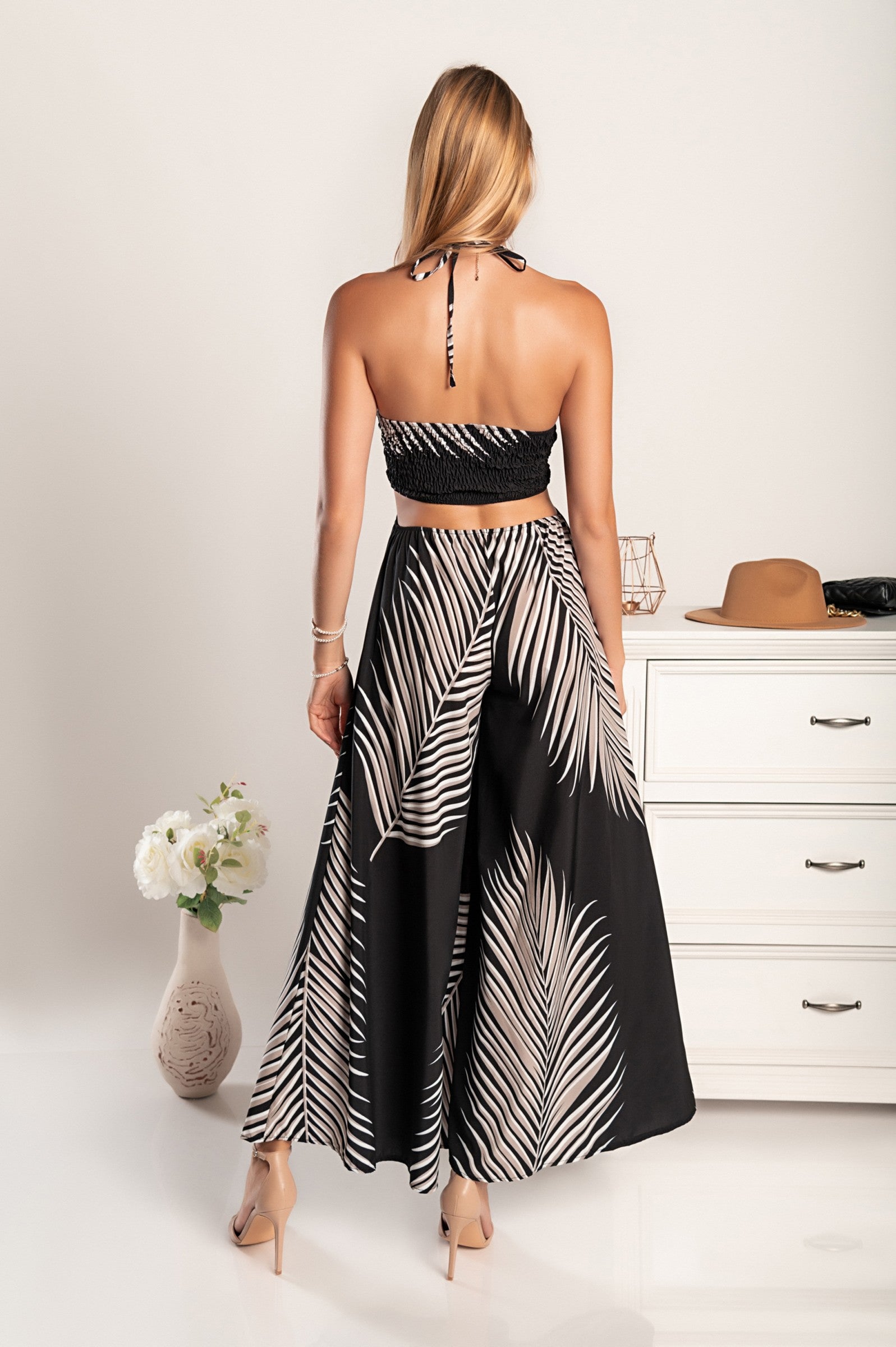 Elegant black jumpsuit with palm leaf print, featuring a plunging neckline, slim straps, and stylish cutouts on the belly and sides.