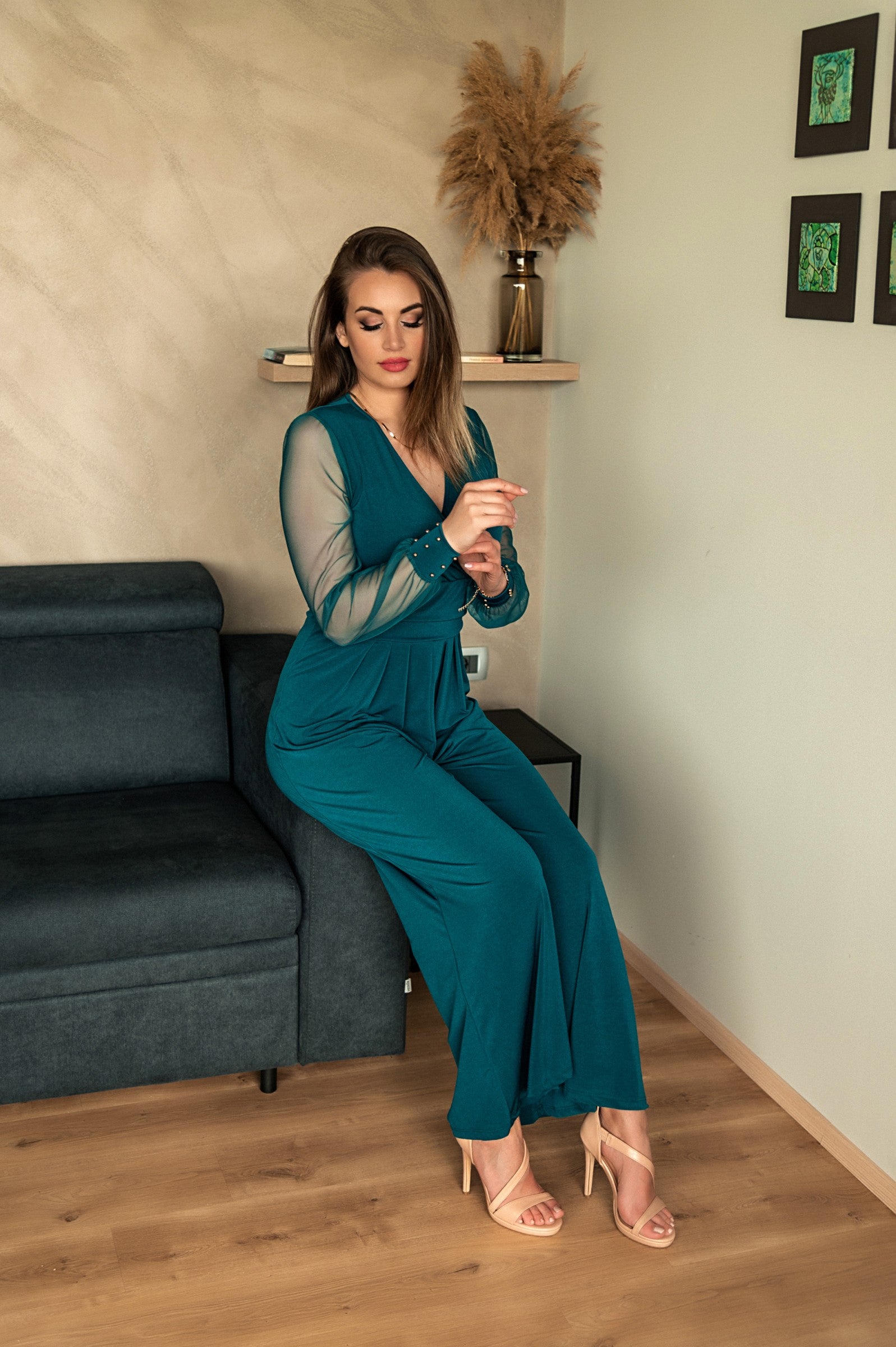 Elegant petrol jumpsuit with V neckline and long transparent sleeves, featuring gold rivets at the wrists.