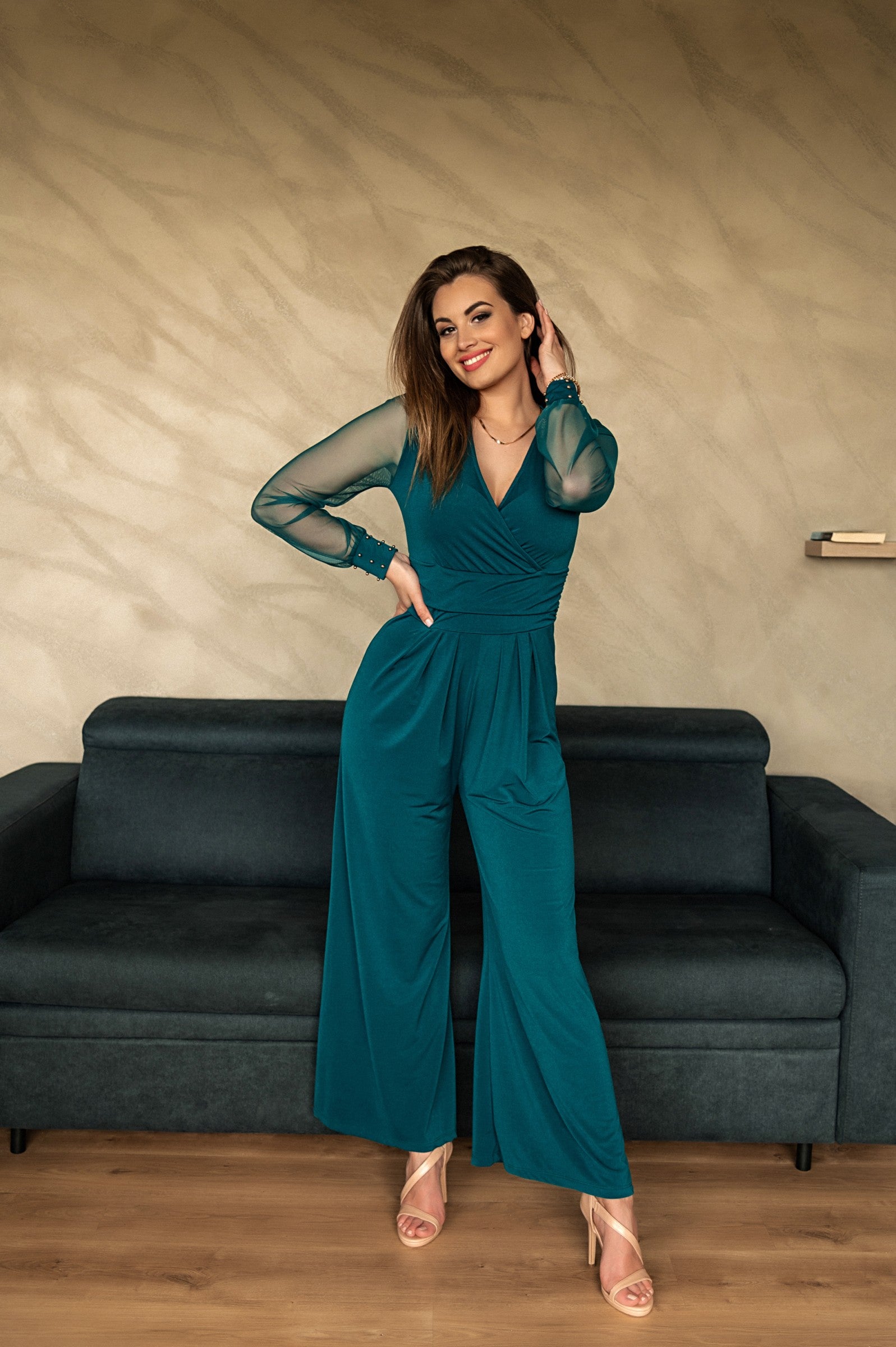 Elegant petrol jumpsuit with V neckline and long transparent sleeves, featuring gold rivets at the wrists.