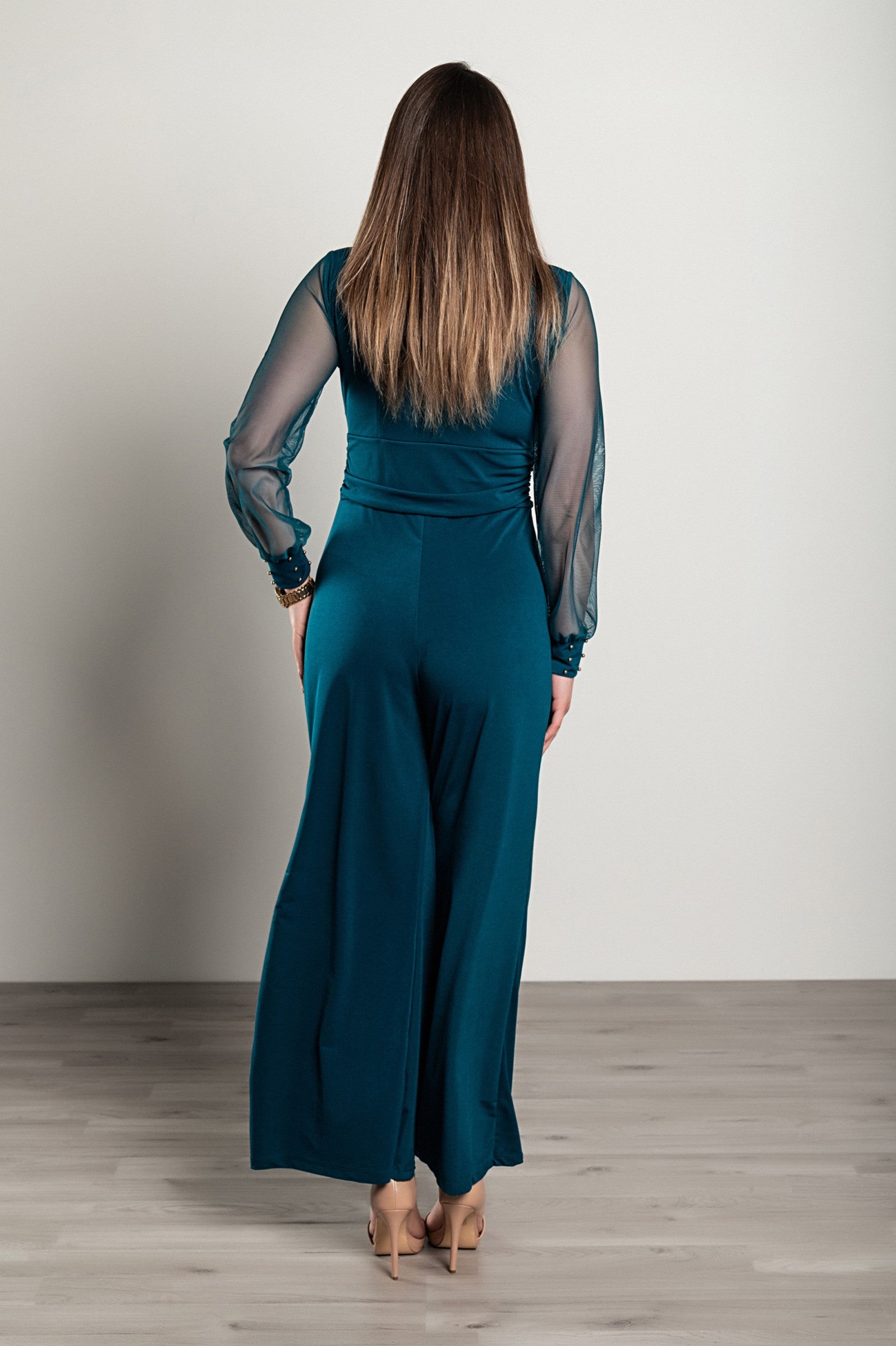 Elegant petrol jumpsuit with V neckline and long transparent sleeves, featuring gold rivets at the wrists.