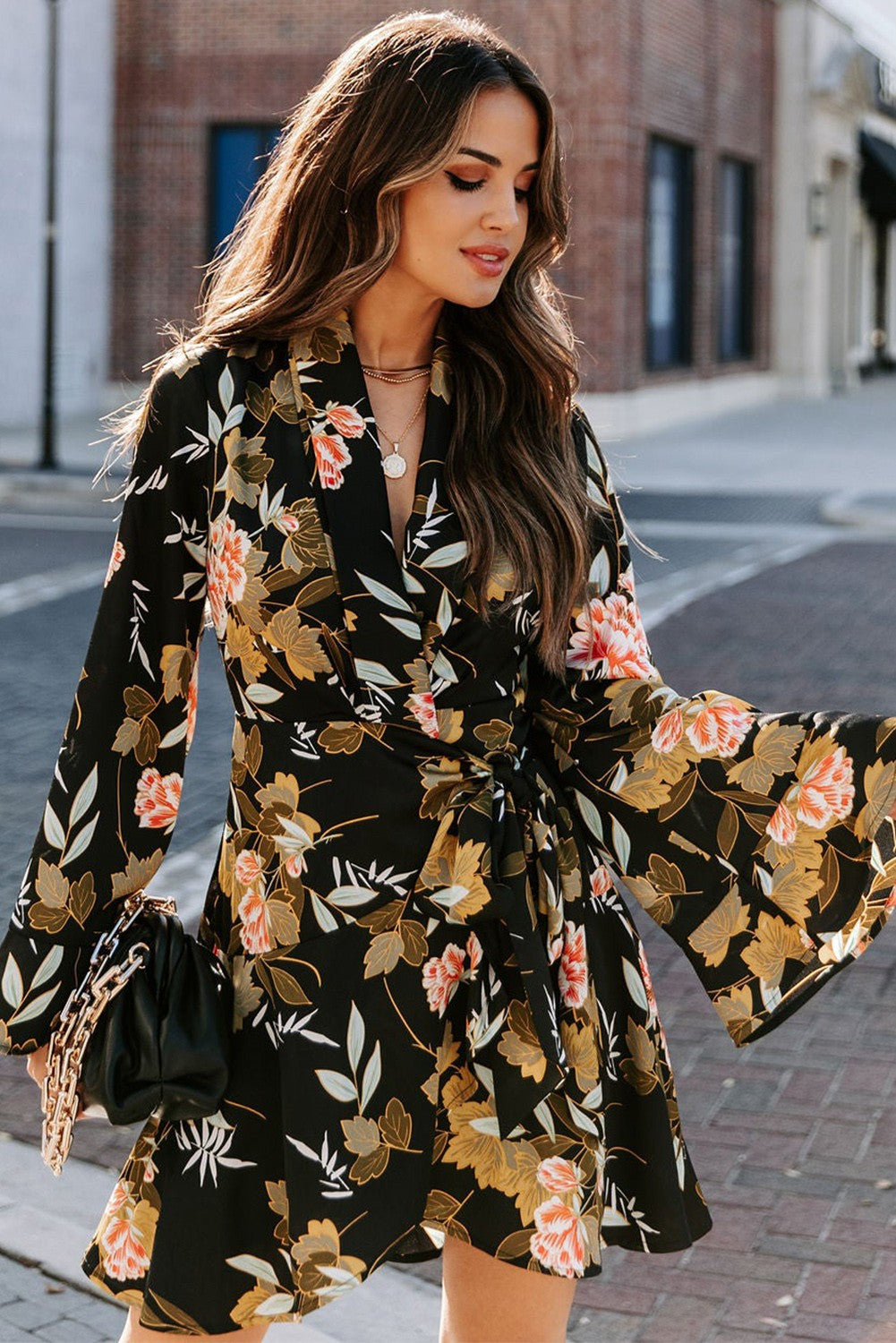 Elegant black mini dress featuring a floral print, wrap neckline, long ruffled sleeves, and a decorative belt.