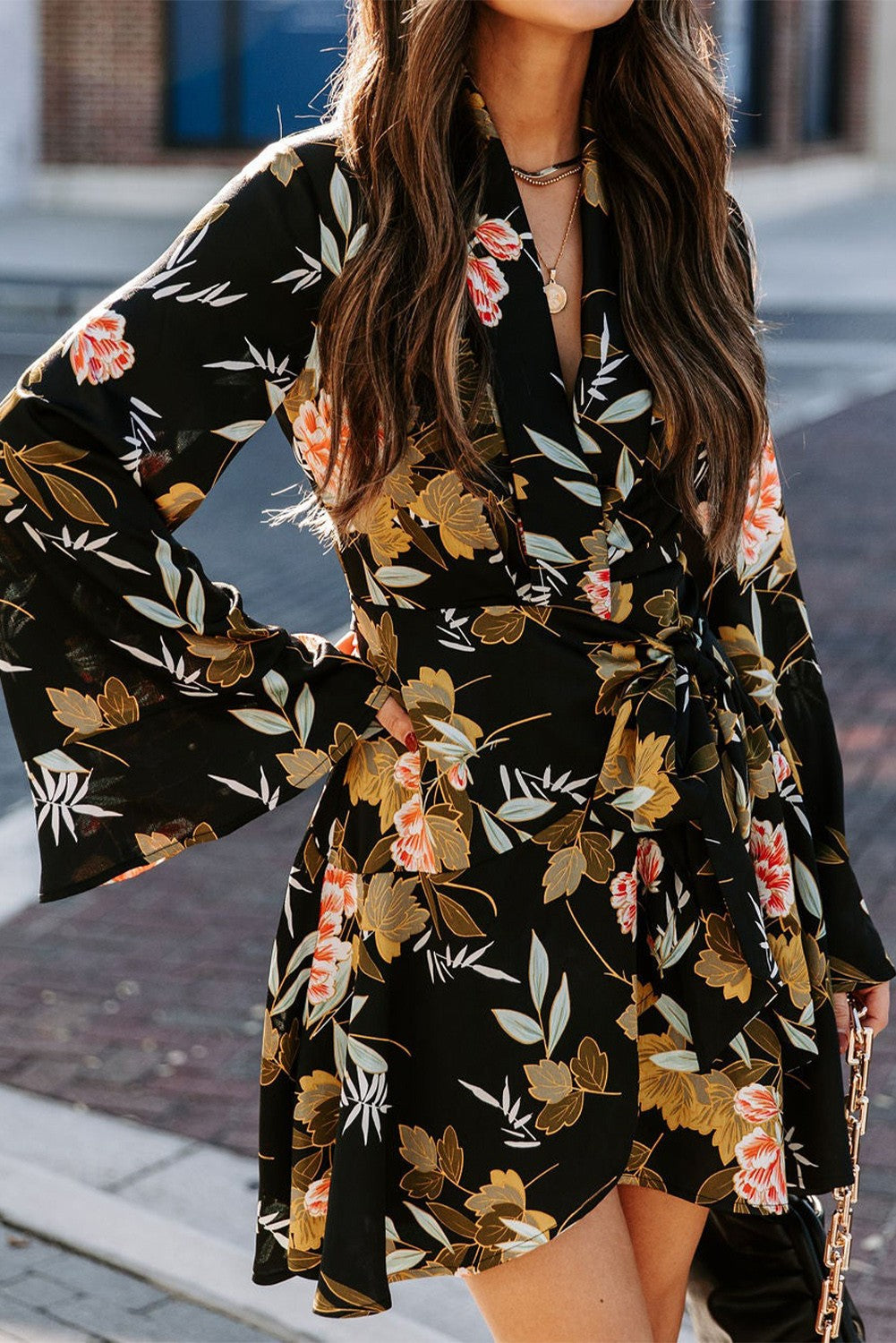 Elegant black mini dress featuring a floral print, wrap neckline, long ruffled sleeves, and a decorative belt.