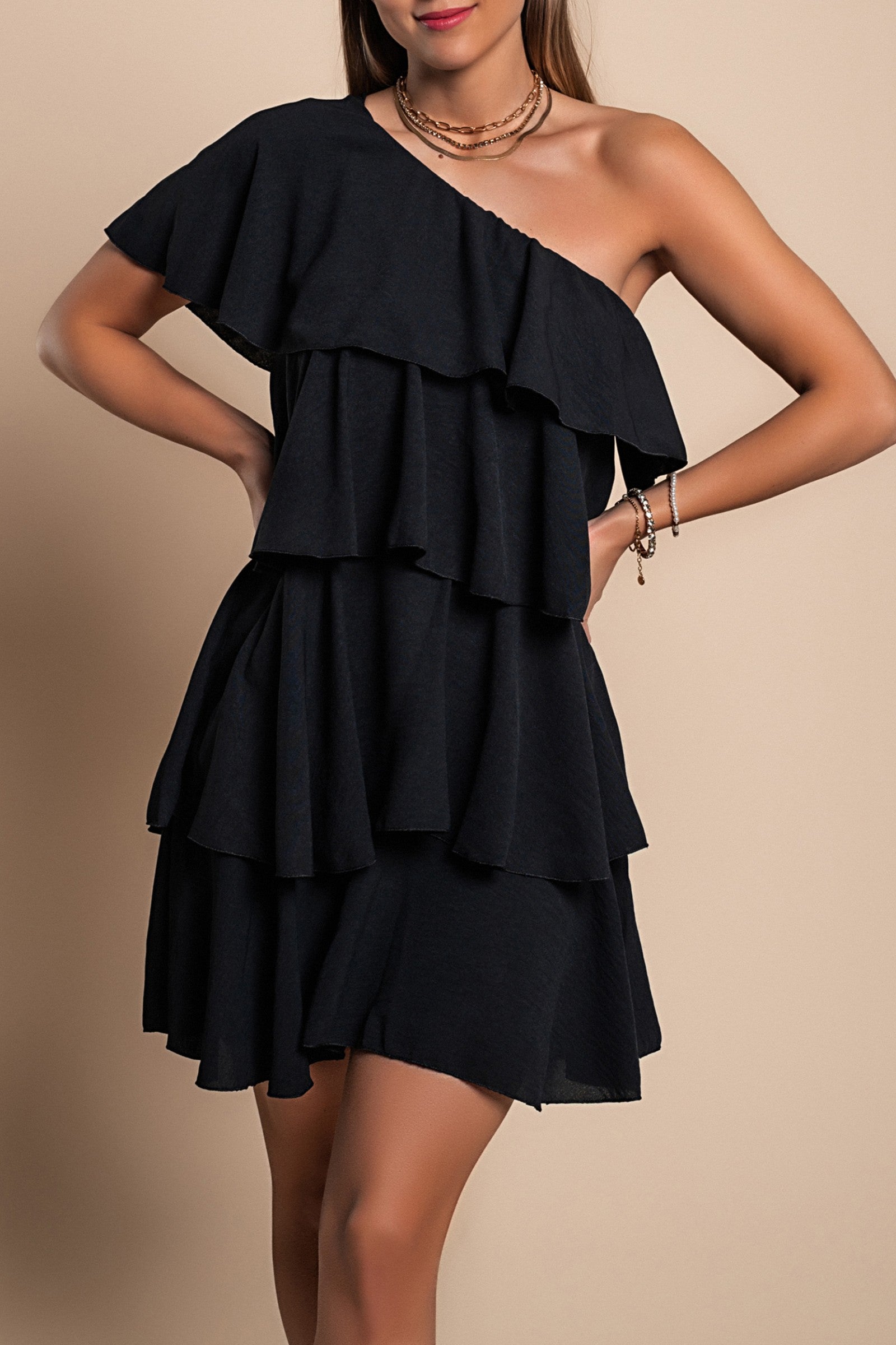 Elegant black mini dress with ruffles, asymmetrical neckline, and single strap, showcasing a loose fit and mid-thigh length.