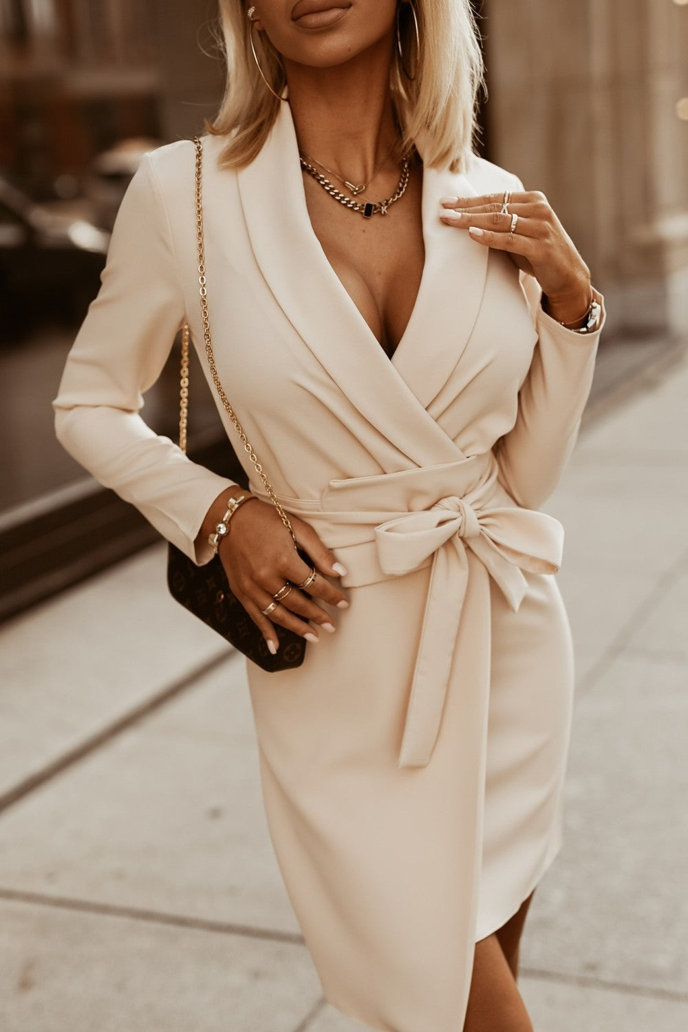 Elegant beige mini dress with wide waist and plunging neckline, featuring long sleeves and a mid-thigh slit.