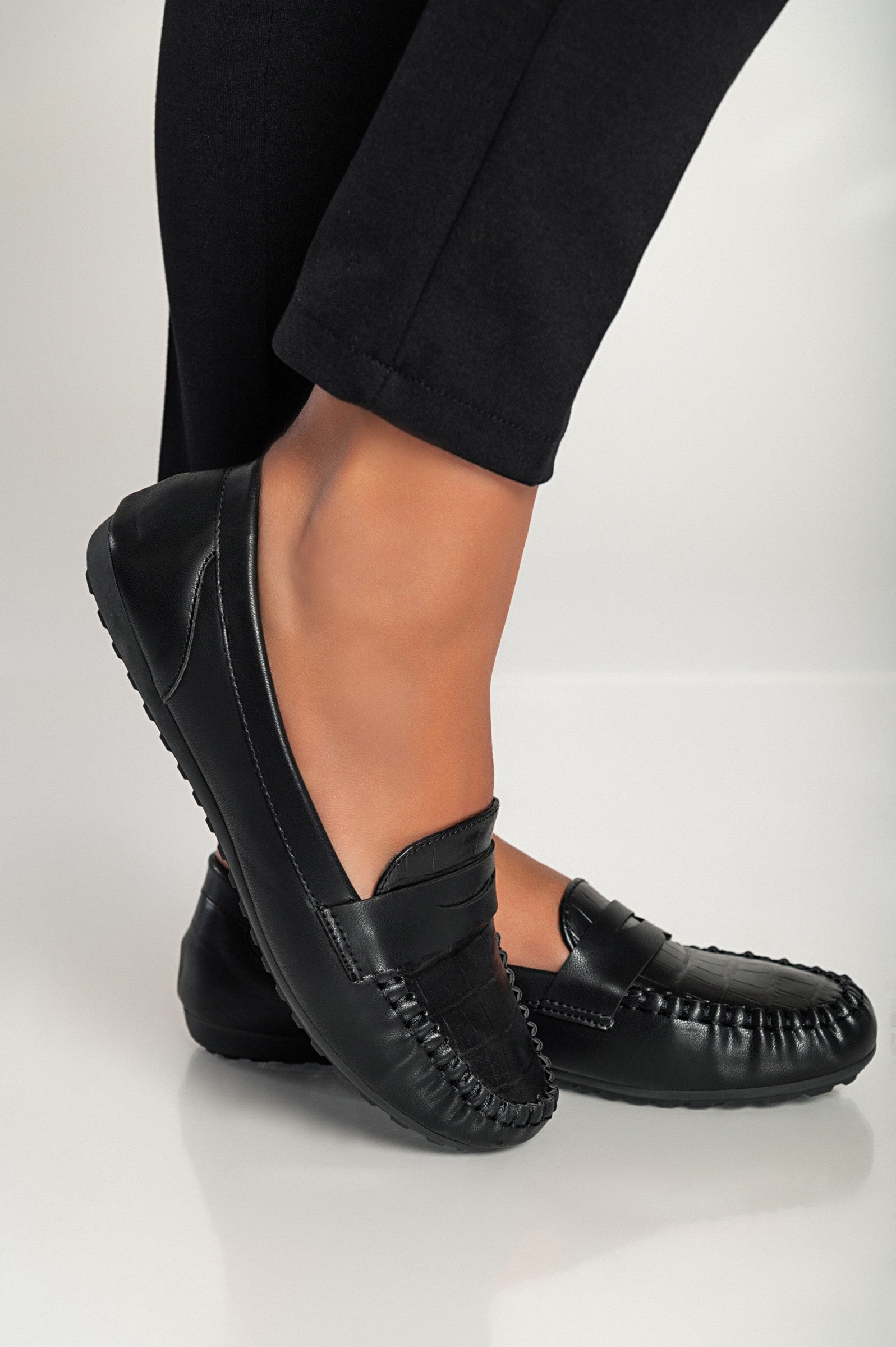 Elegant black moccasins featuring a crocodile print design, with a flat sole and decorative details, perfect for stylish comfort.