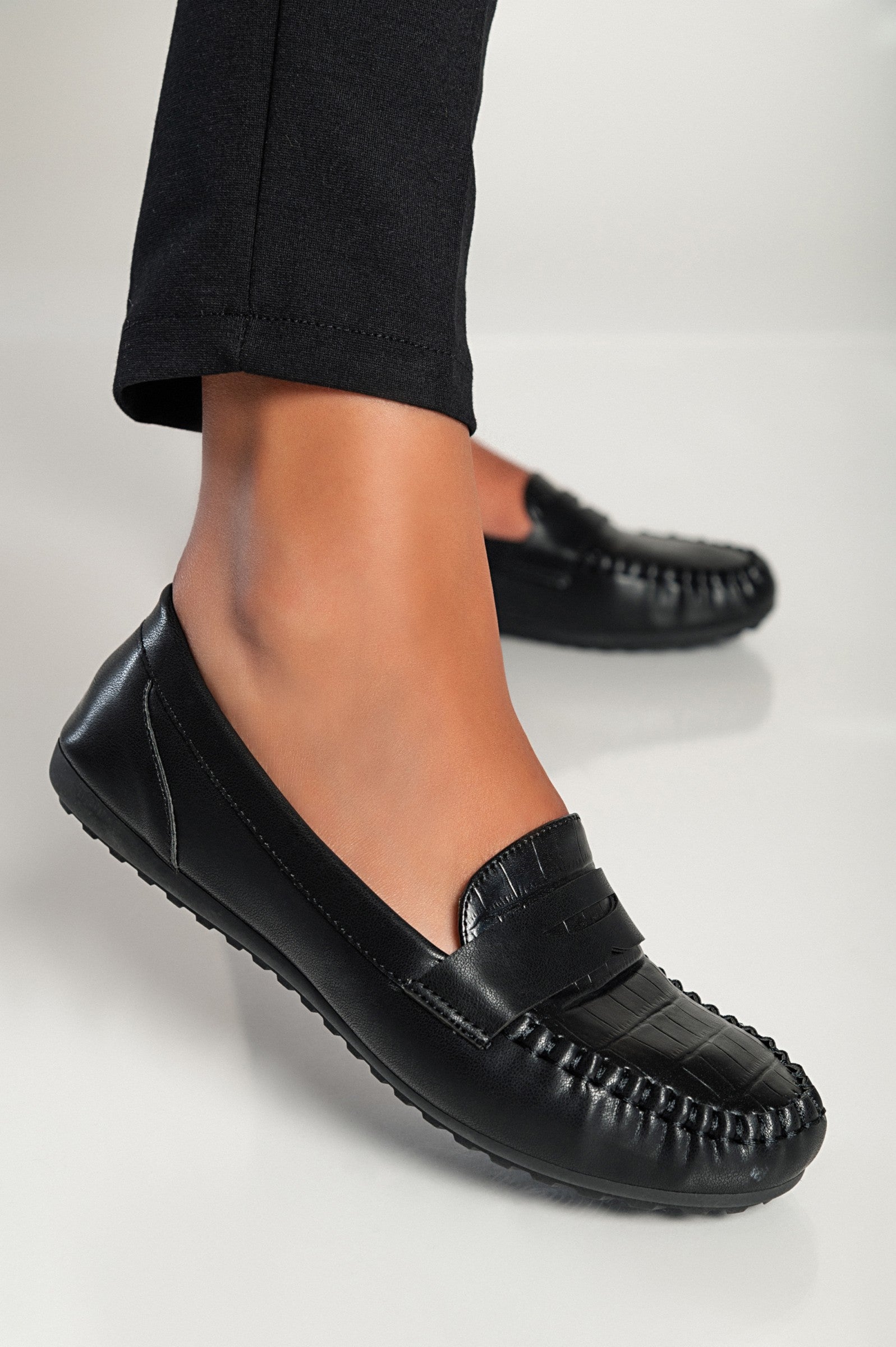 Elegant black moccasins featuring a crocodile print design, with a flat sole and decorative details, perfect for stylish comfort.