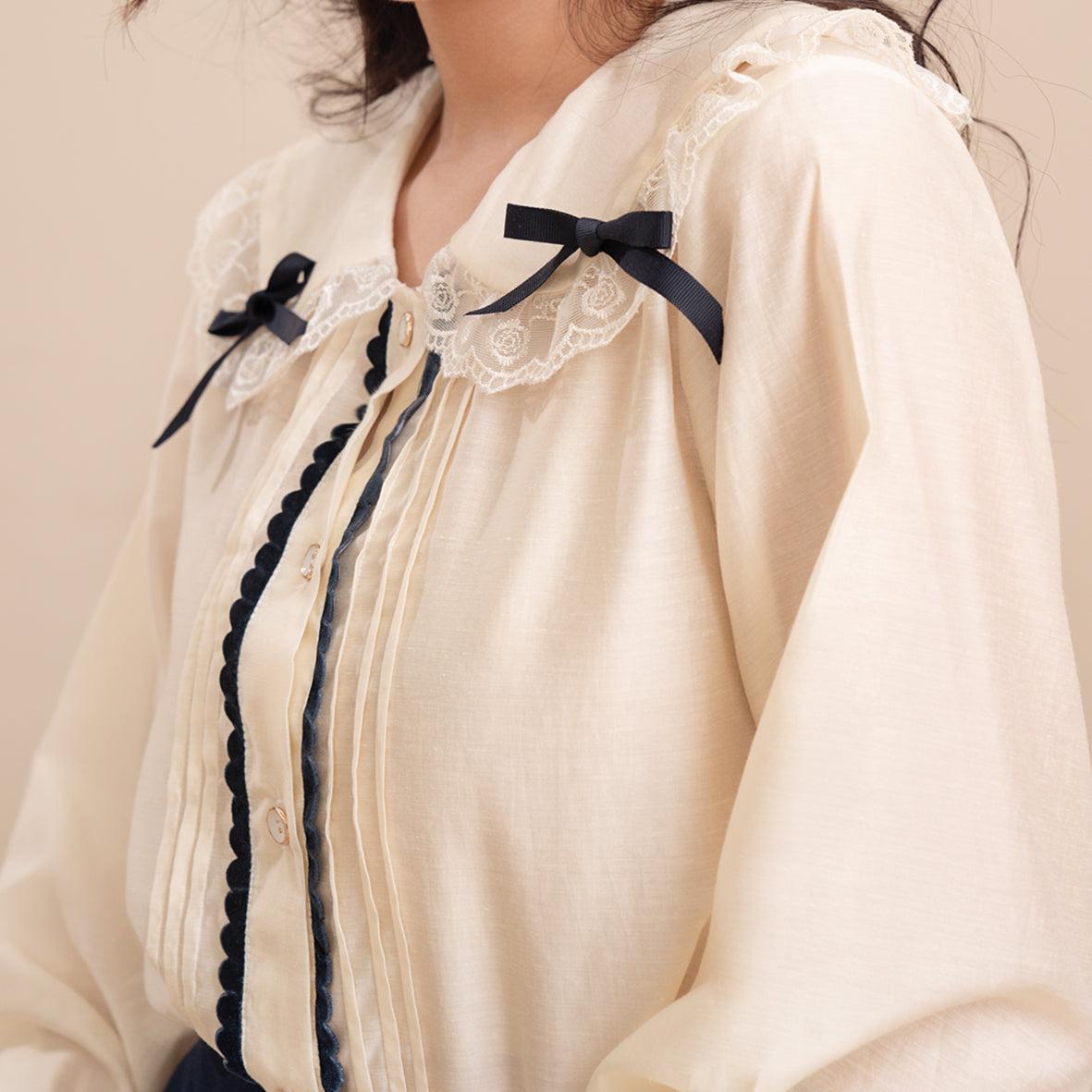 Elegant Enora Shirt made of soft silk, featuring an A-line shape, round collar, lace and bow accents, and pleated bodice with velvet cord.