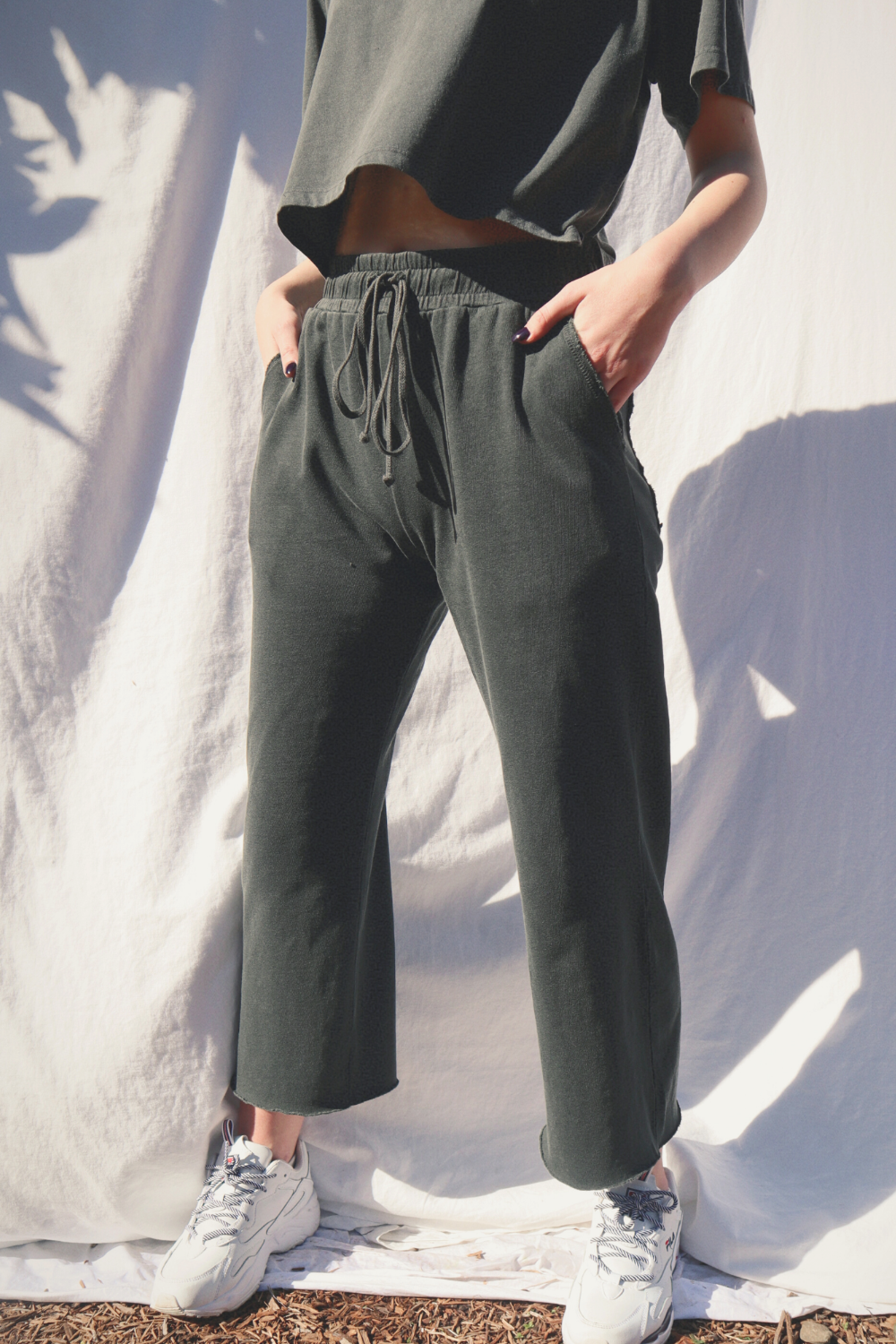 A pair of slouchy, cropped Everyday Pants in washed black with a drawstring waist and pockets, showcasing a relaxed fit and flared raw cut hem.