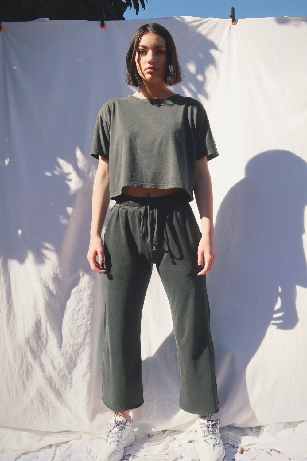 A pair of slouchy, cropped Everyday Pants in washed black with a drawstring waist and pockets, showcasing a relaxed fit and flared raw cut hem.