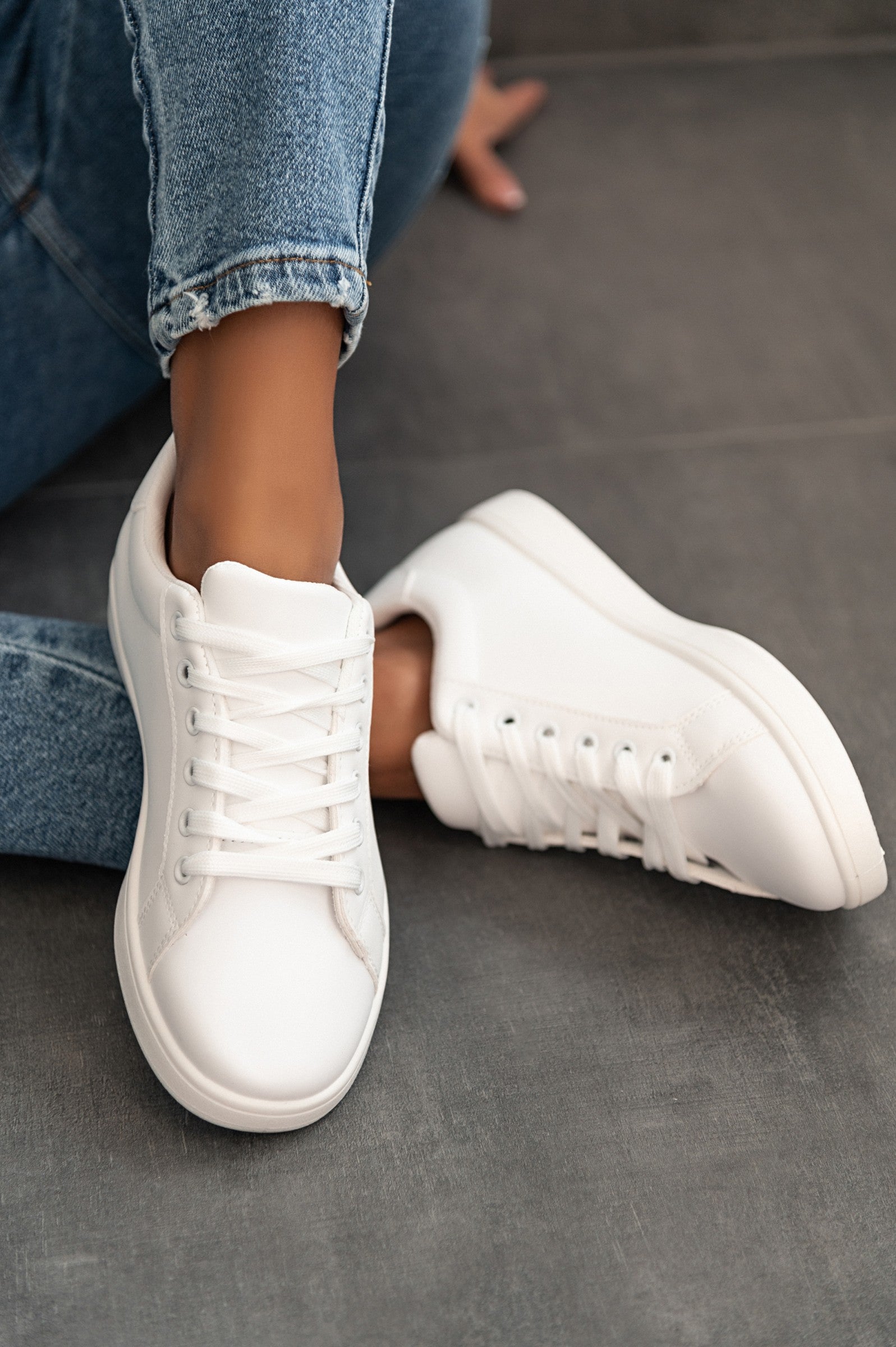 White fashion sneakers with flat sole, round toe, and bow closure, made of synthetic leather.