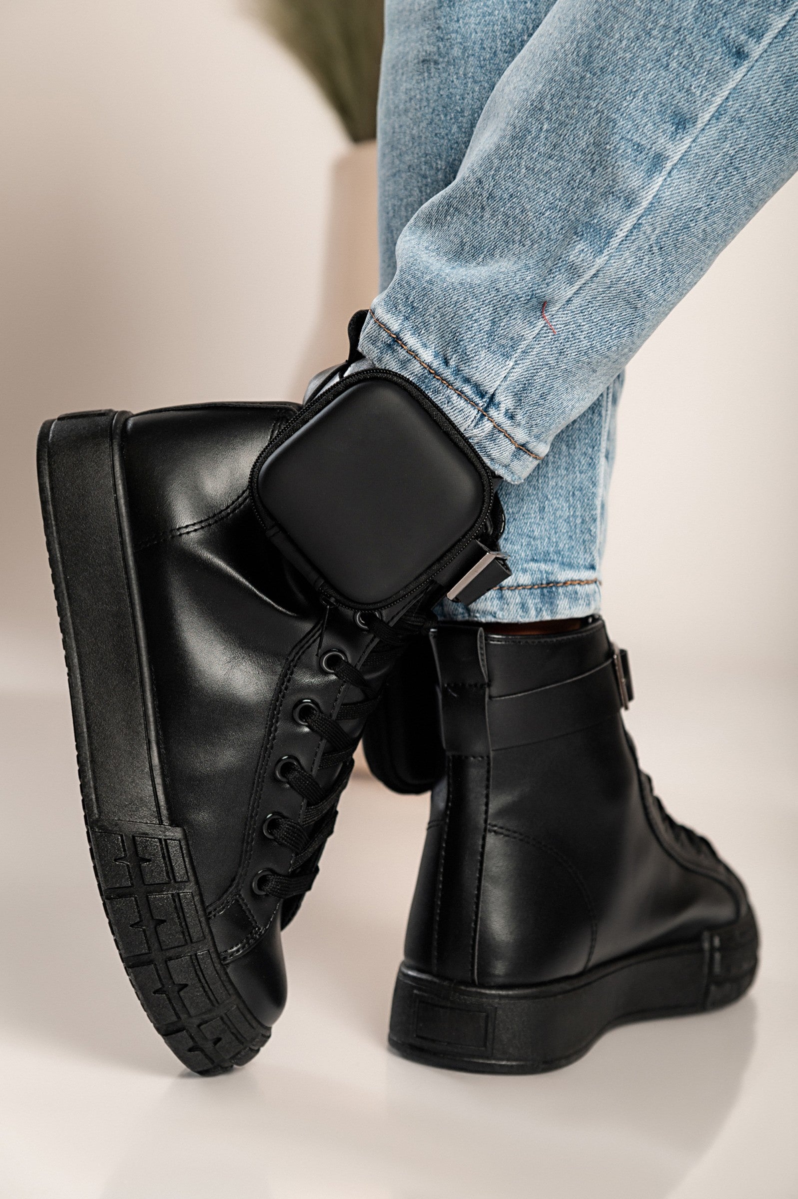 A pair of stylish black faux leather fashion sneakers with a raised sole and a removable mini bag detail around the ankle.