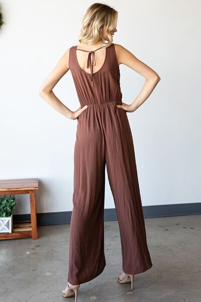 A stylish woman wearing the First Love Tie Back Sleeveless Slit Wide Leg Jumpsuit, showcasing its unique tie back design and flirty leg slit.