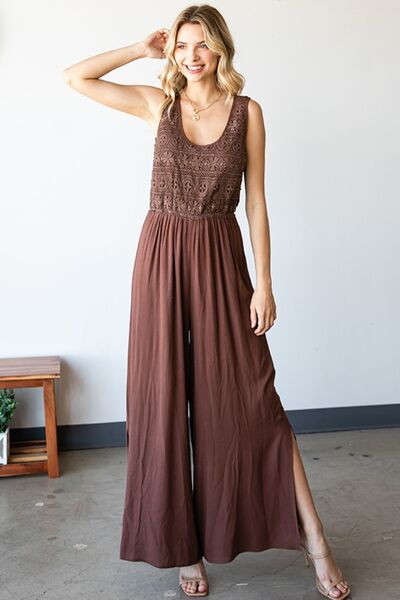 A stylish woman wearing the First Love Tie Back Sleeveless Slit Wide Leg Jumpsuit, showcasing its unique tie back design and flirty leg slit.