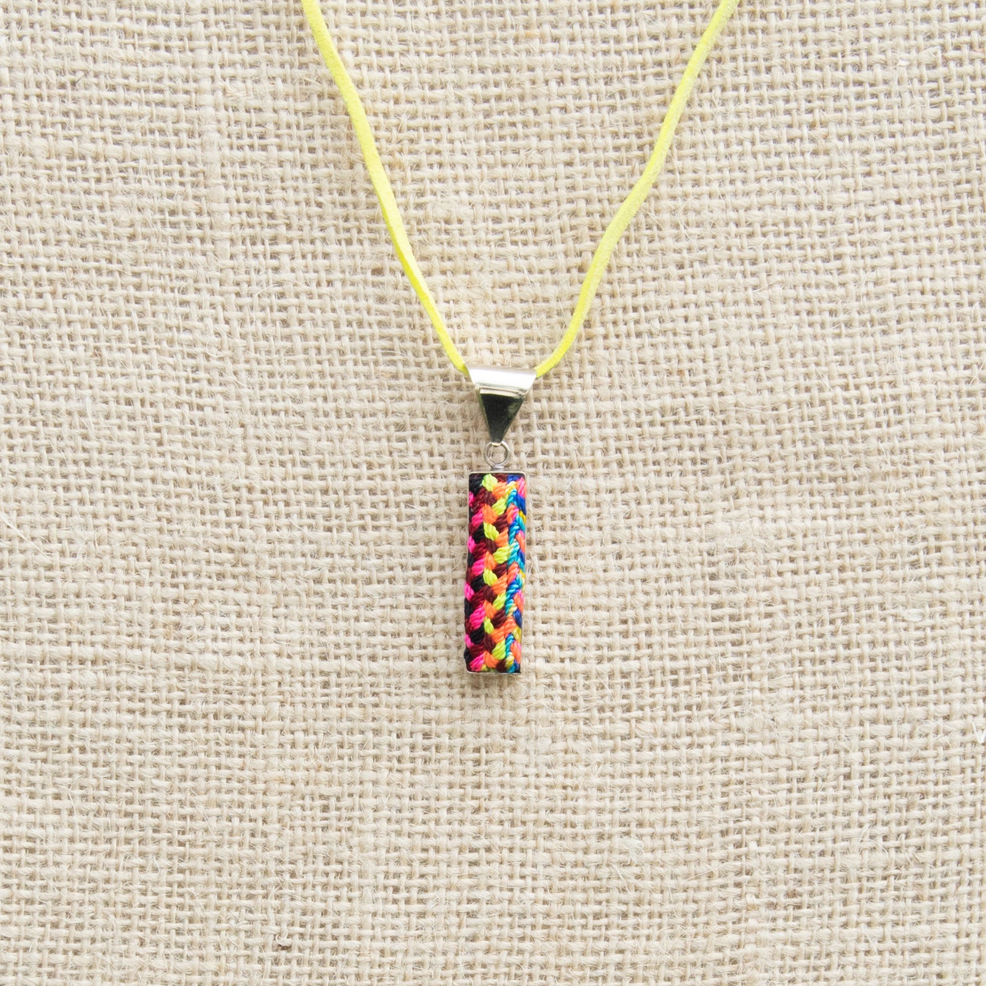 A colorful Folk Long Pendant Necklace featuring unique hand-embroidered patterns by artisans from Chiapas, Mexico, displayed elegantly on a neutral background.