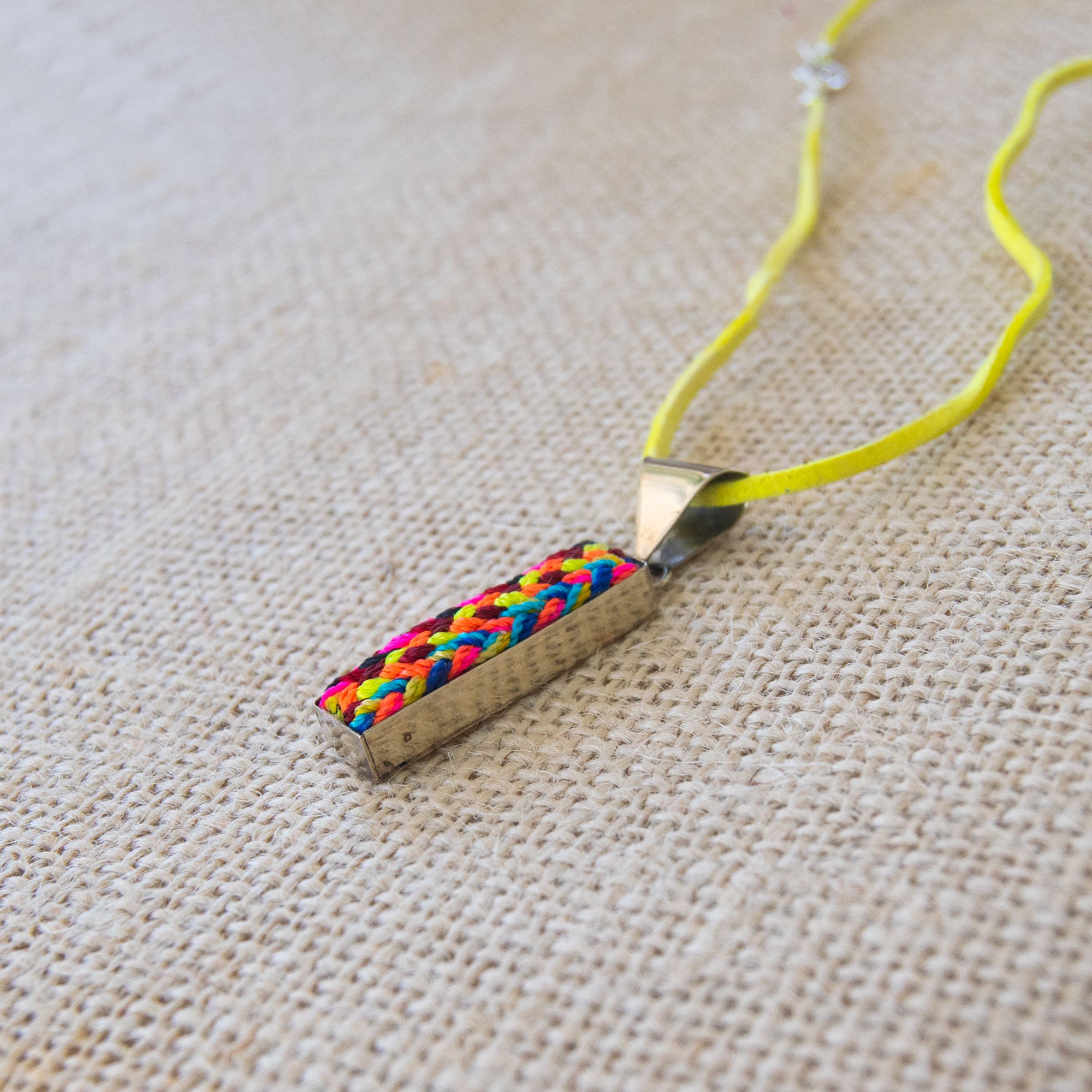 A colorful Folk Long Pendant Necklace featuring unique hand-embroidered patterns by artisans from Chiapas, Mexico, displayed elegantly on a neutral background.