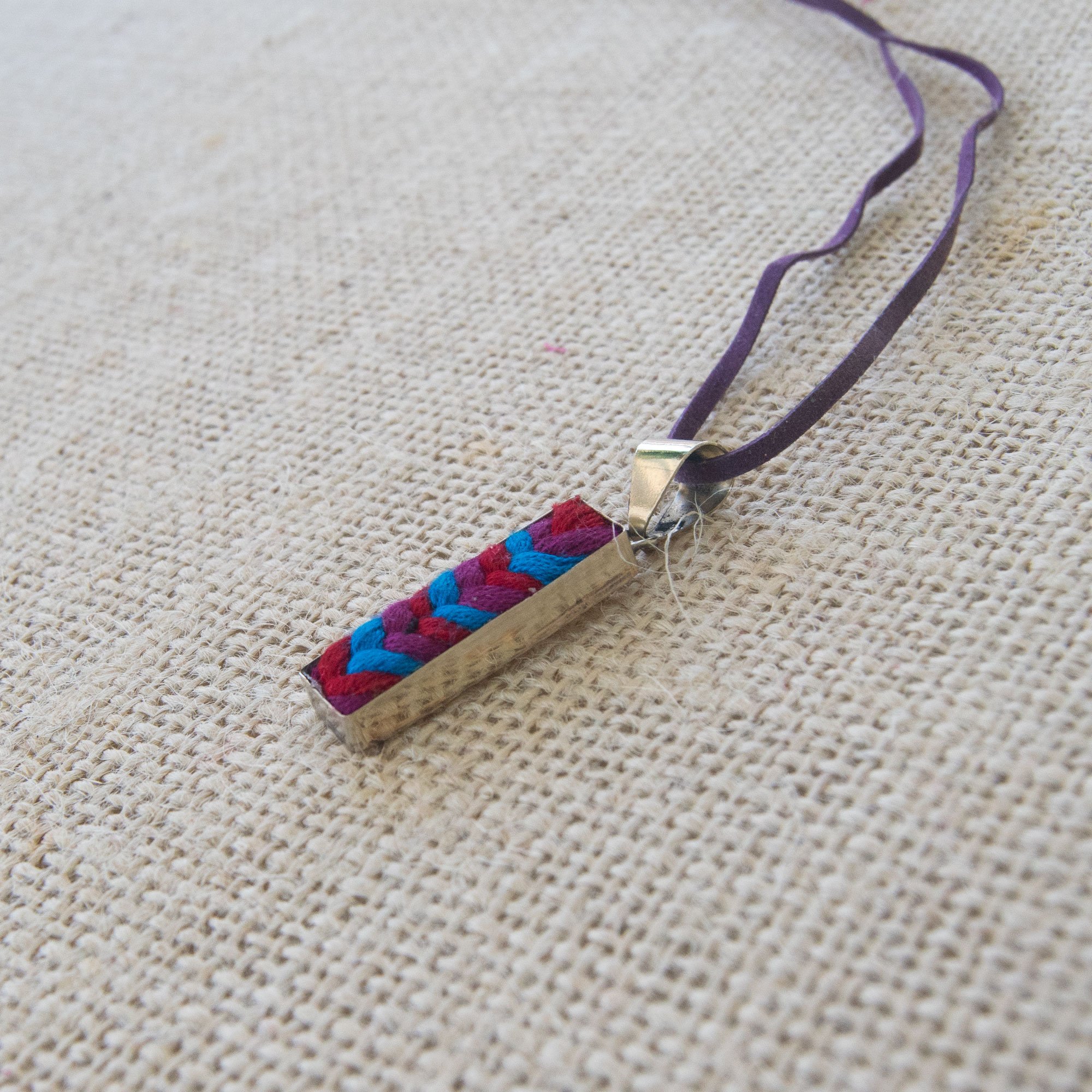 A colorful Folk Long Pendant Necklace featuring unique hand-embroidered patterns by artisans from Chiapas, Mexico, displayed elegantly on a neutral background.