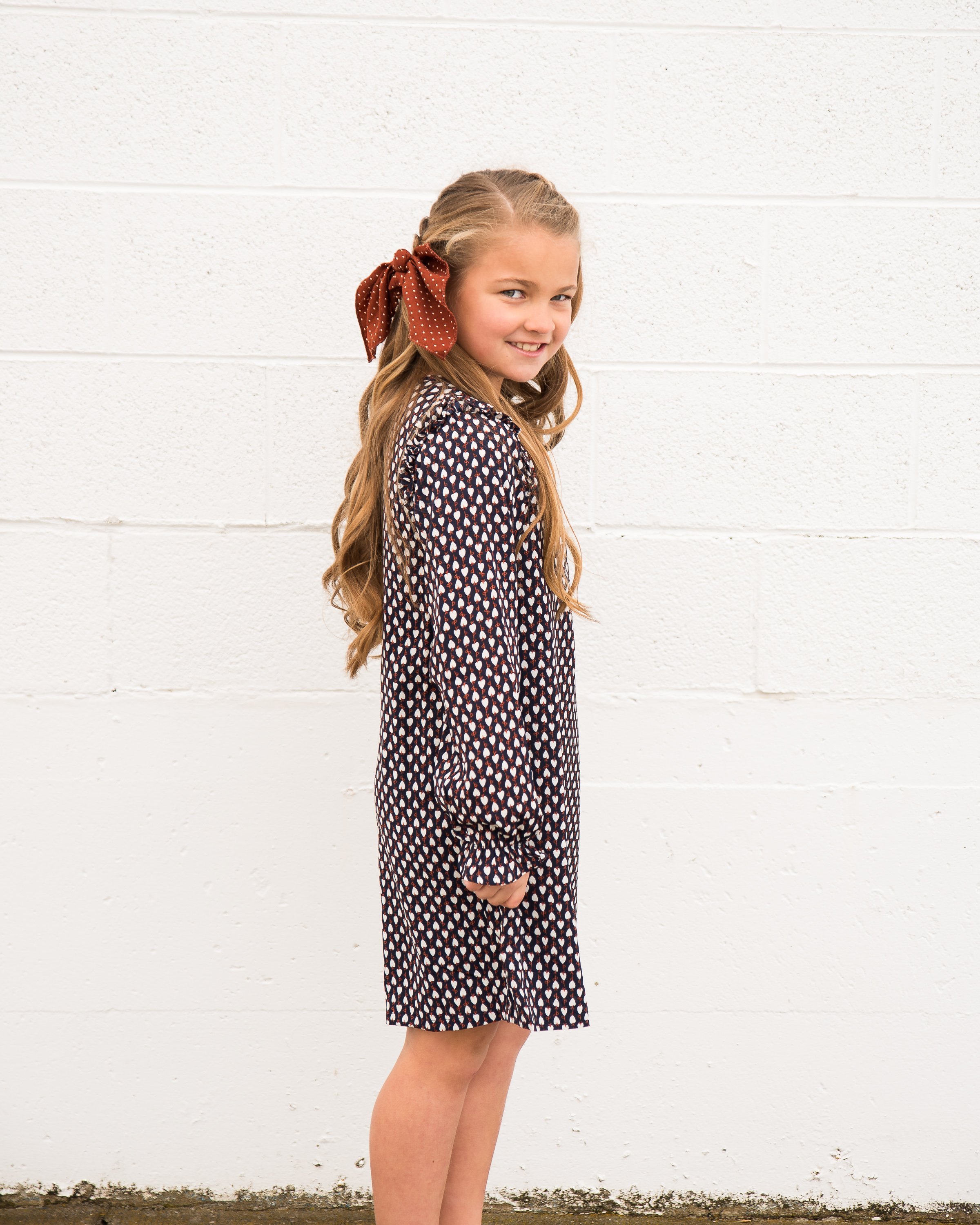 A cute navy geometric print shift dress for little girls featuring ruffle shoulders and long sleeves.