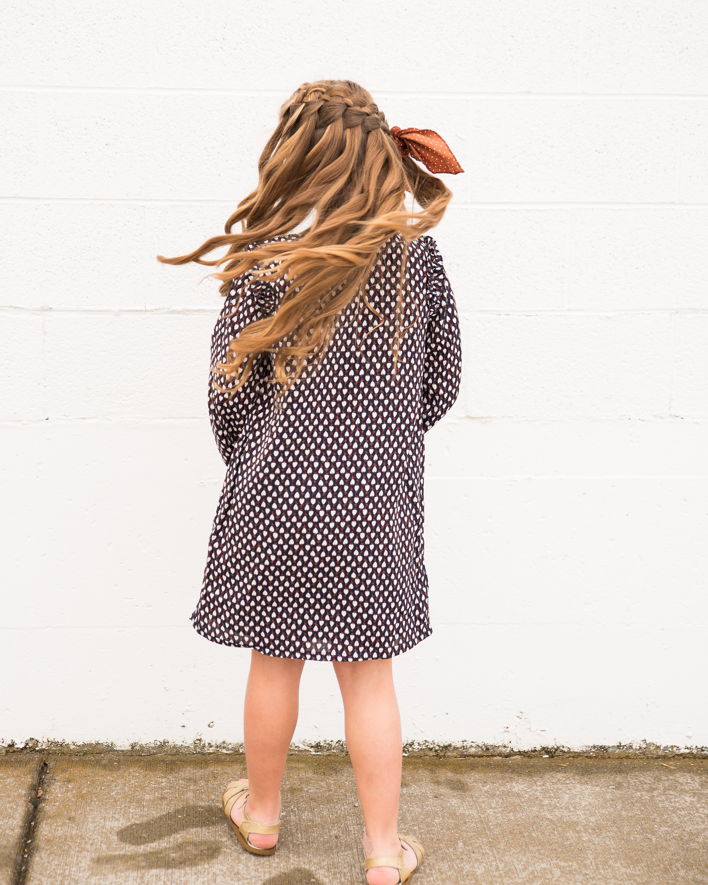 A cute navy geometric print shift dress for little girls featuring ruffle shoulders and long sleeves.