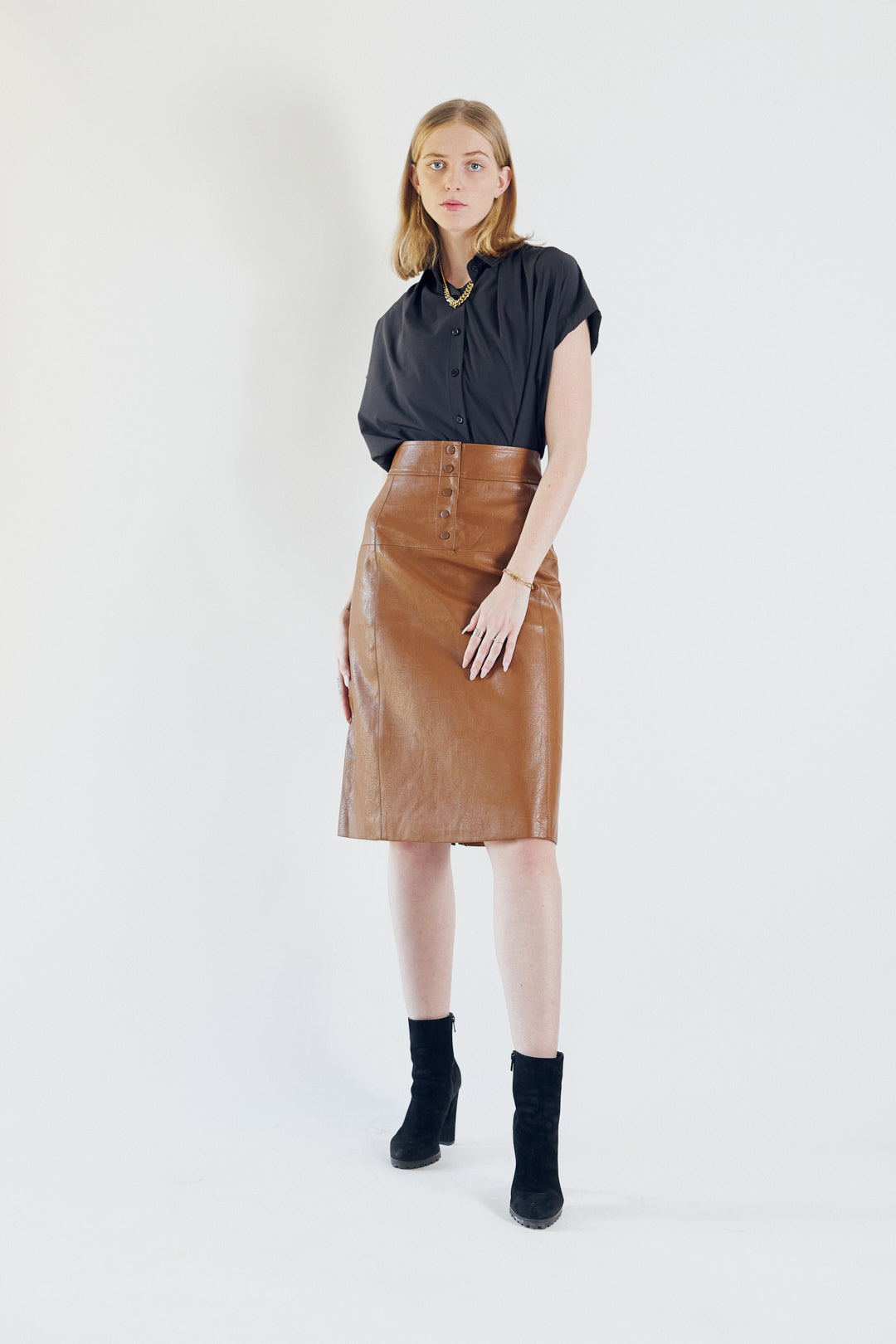 Glossy brown vegan leather pencil skirt with front button detail, knee-length design, and stylish silhouette.