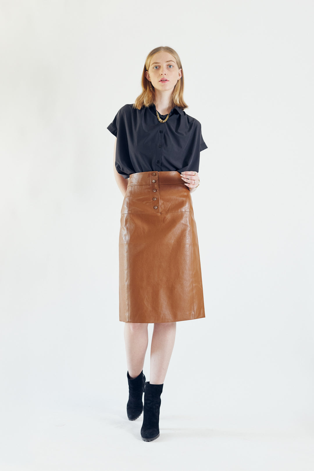 Glossy brown vegan leather pencil skirt with front button detail, knee-length design, and stylish silhouette.