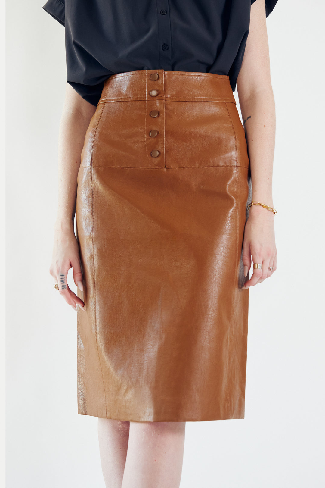 Glossy brown vegan leather pencil skirt with front button detail, knee-length design, and stylish silhouette.