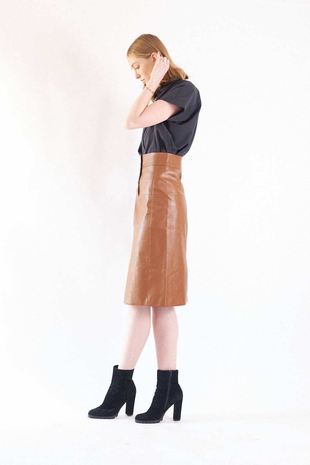 Glossy brown vegan leather pencil skirt with front button detail, knee-length design, and stylish silhouette.