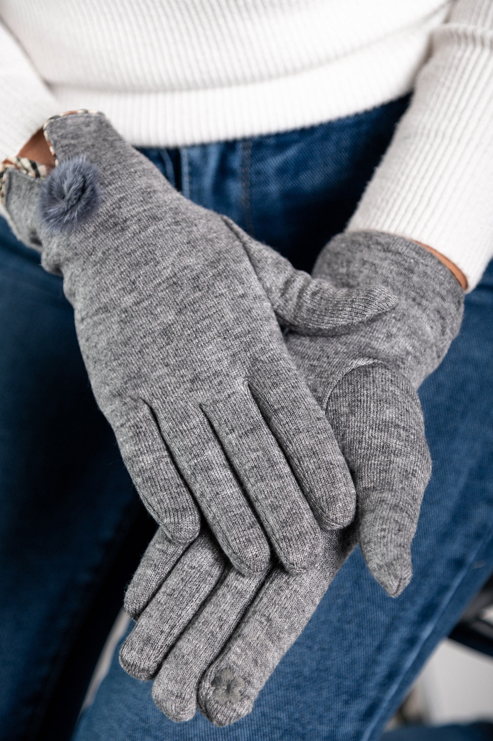 Gray gloves with decorative faux fur pompom, showcasing soft fabric and stylish design.