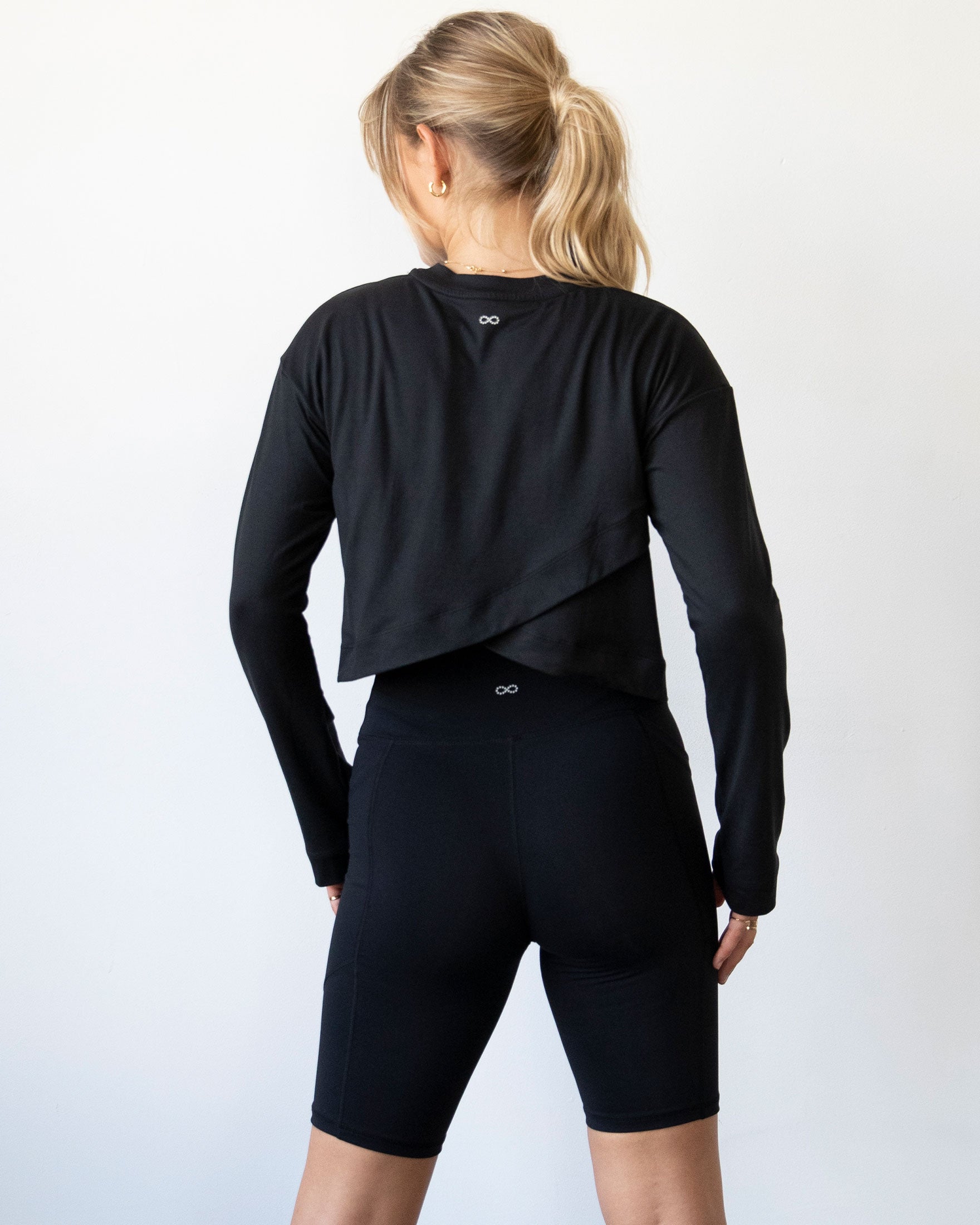 A stylish woman wearing the Go With The Flow Crop Long Sleeve with bell sleeves and a criss-cross back, paired with leggings.