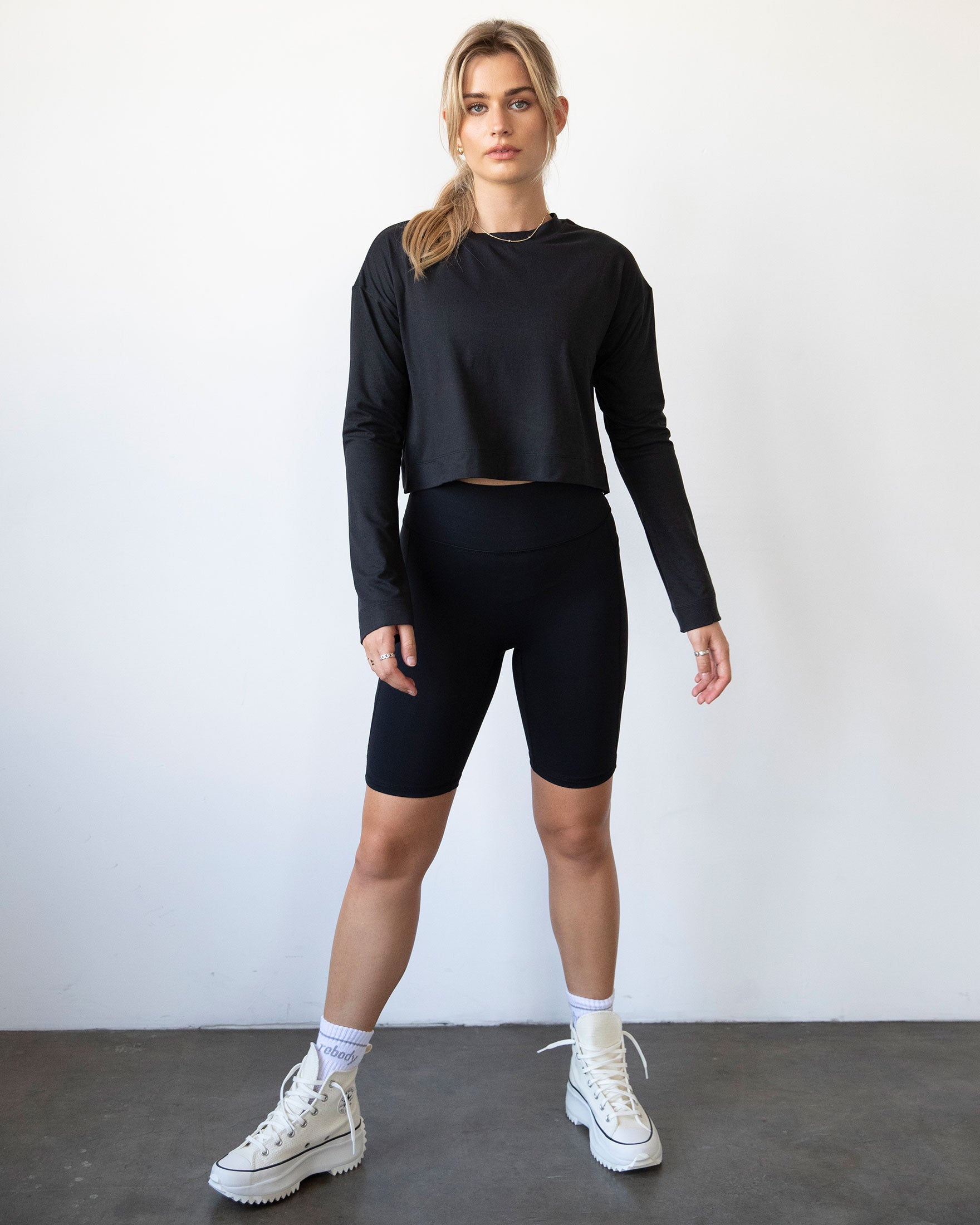 A stylish woman wearing the Go With The Flow Crop Long Sleeve with bell sleeves and a criss-cross back, paired with leggings.