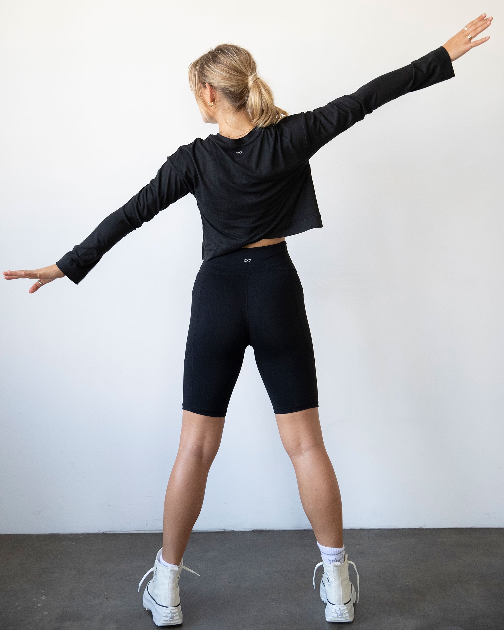 A stylish woman wearing the Go With The Flow Crop Long Sleeve with bell sleeves and a criss-cross back, paired with leggings.