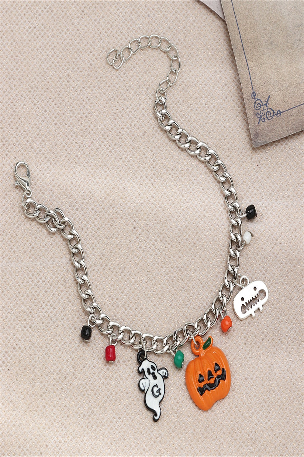 A Halloween charm bracelet and necklace set featuring pumpkin and ghost charms, made from alloy and resin, displayed on a festive background.