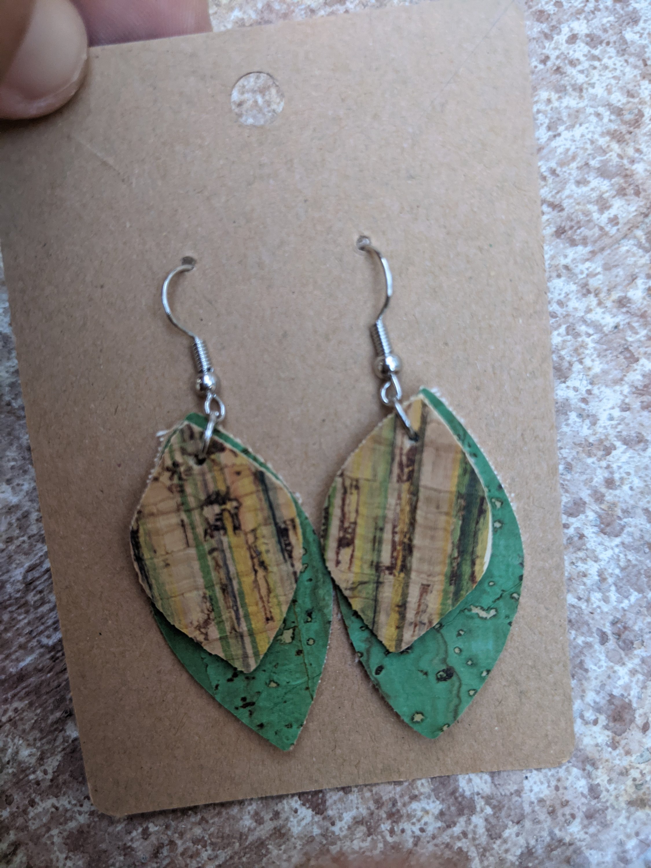 Handmade light green cork earrings featuring a delicate leaf filigree charm, showcasing their unique design and lightweight nature.