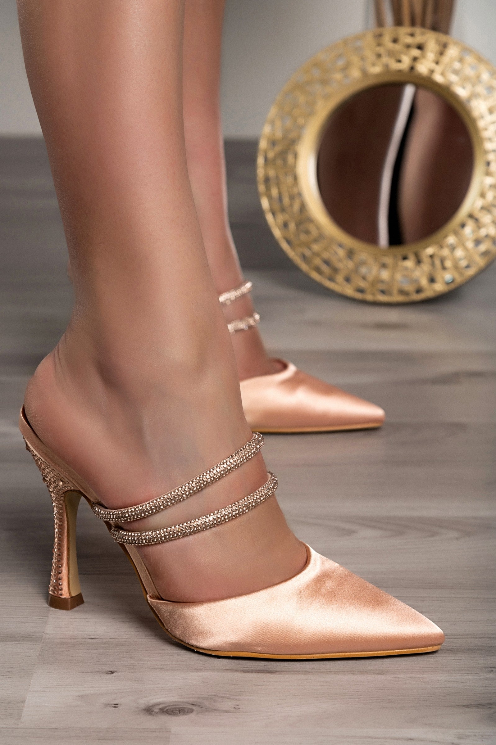 Beige heeled shoes with rhinestone straps and pointed toe, featuring a thin heel for a stylish look.