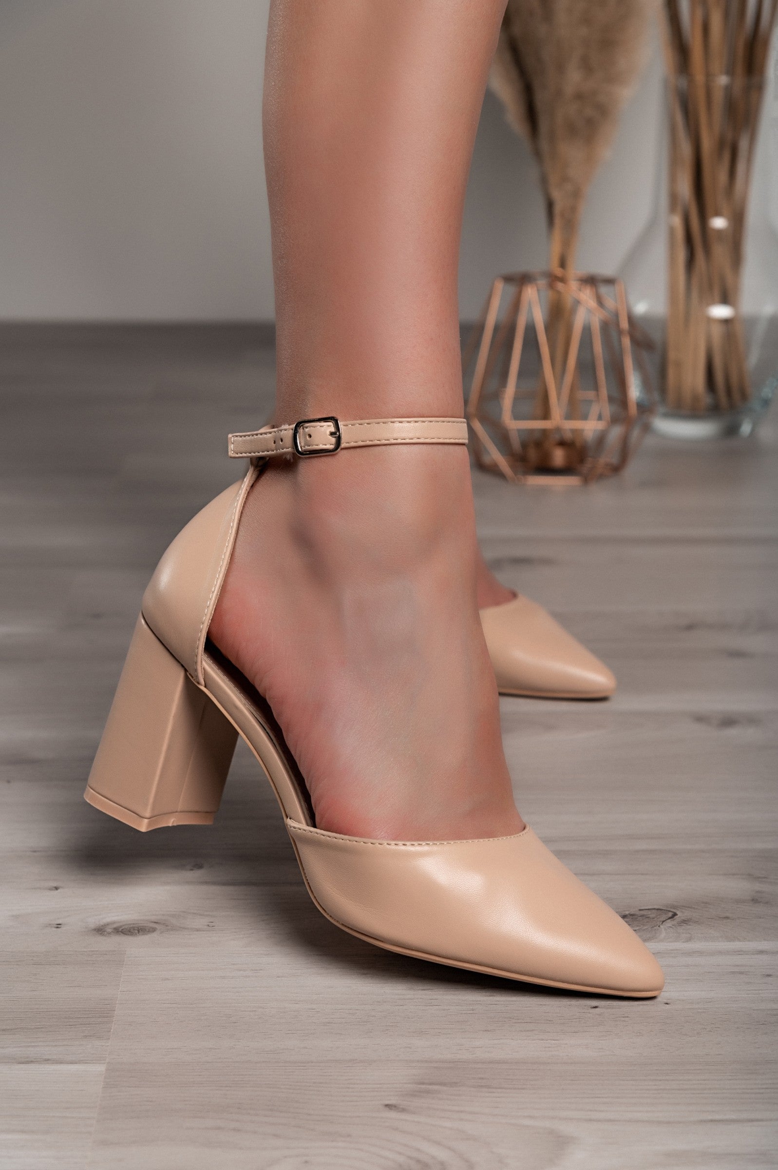 Beige high-heeled shoes with pointed toe and square heel, featuring a buckle strap around the ankle.