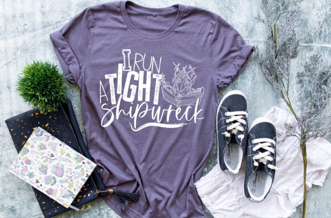 A white graphic design featuring the phrase 'I Run A Tight Shipwreck' on a colorful tee or tank top.