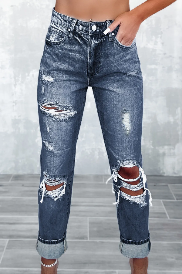 A pair of blue jeans with ripped details, featuring a high waist, button and zipper closure, and side pockets, laid flat on a surface.