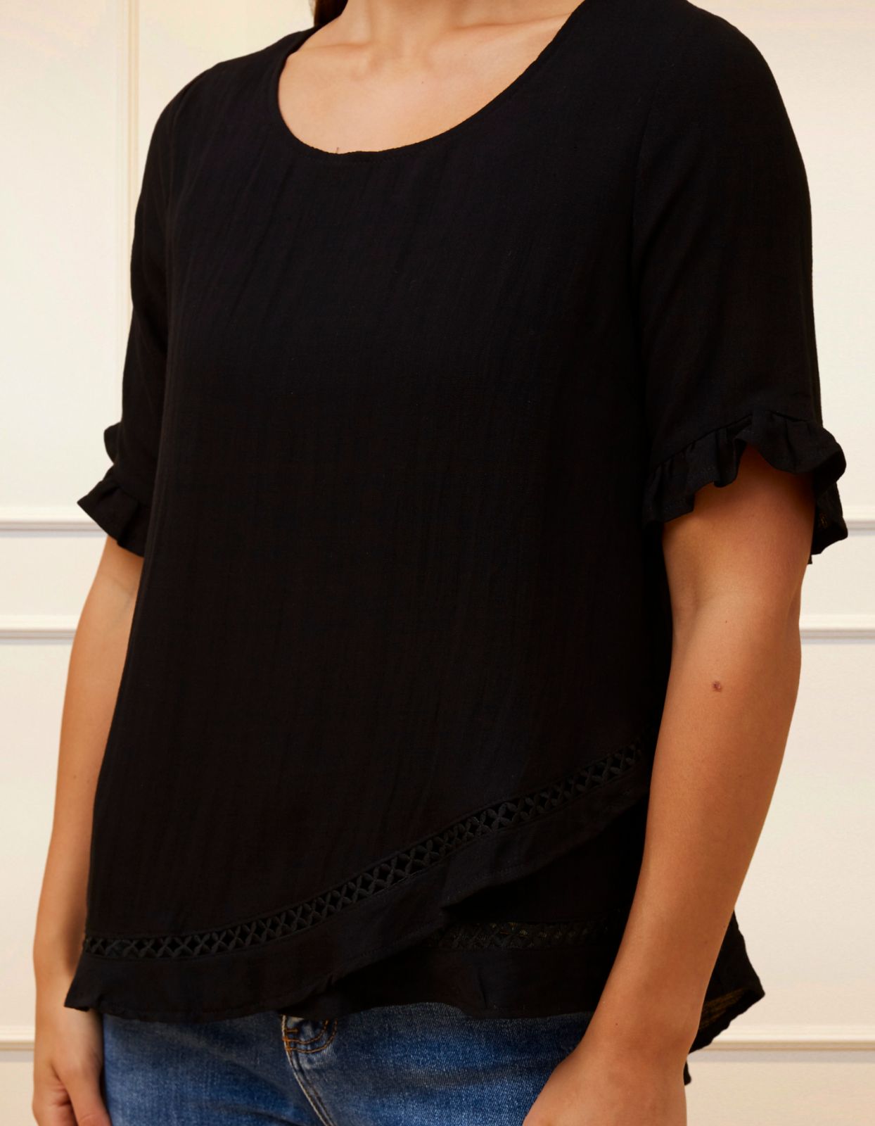 Jessy Top in Black featuring a relaxed fit, crossover hemline, and frilled cuffs, perfect for versatile styling.