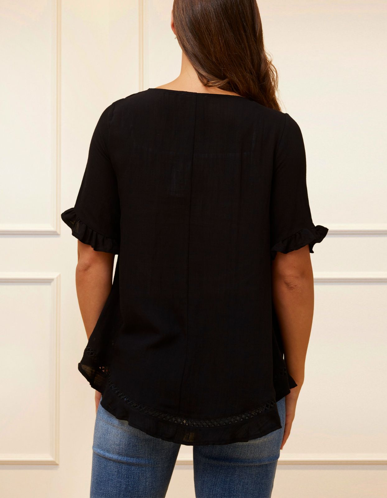 Jessy Top in Black featuring a relaxed fit, crossover hemline, and frilled cuffs, perfect for versatile styling.