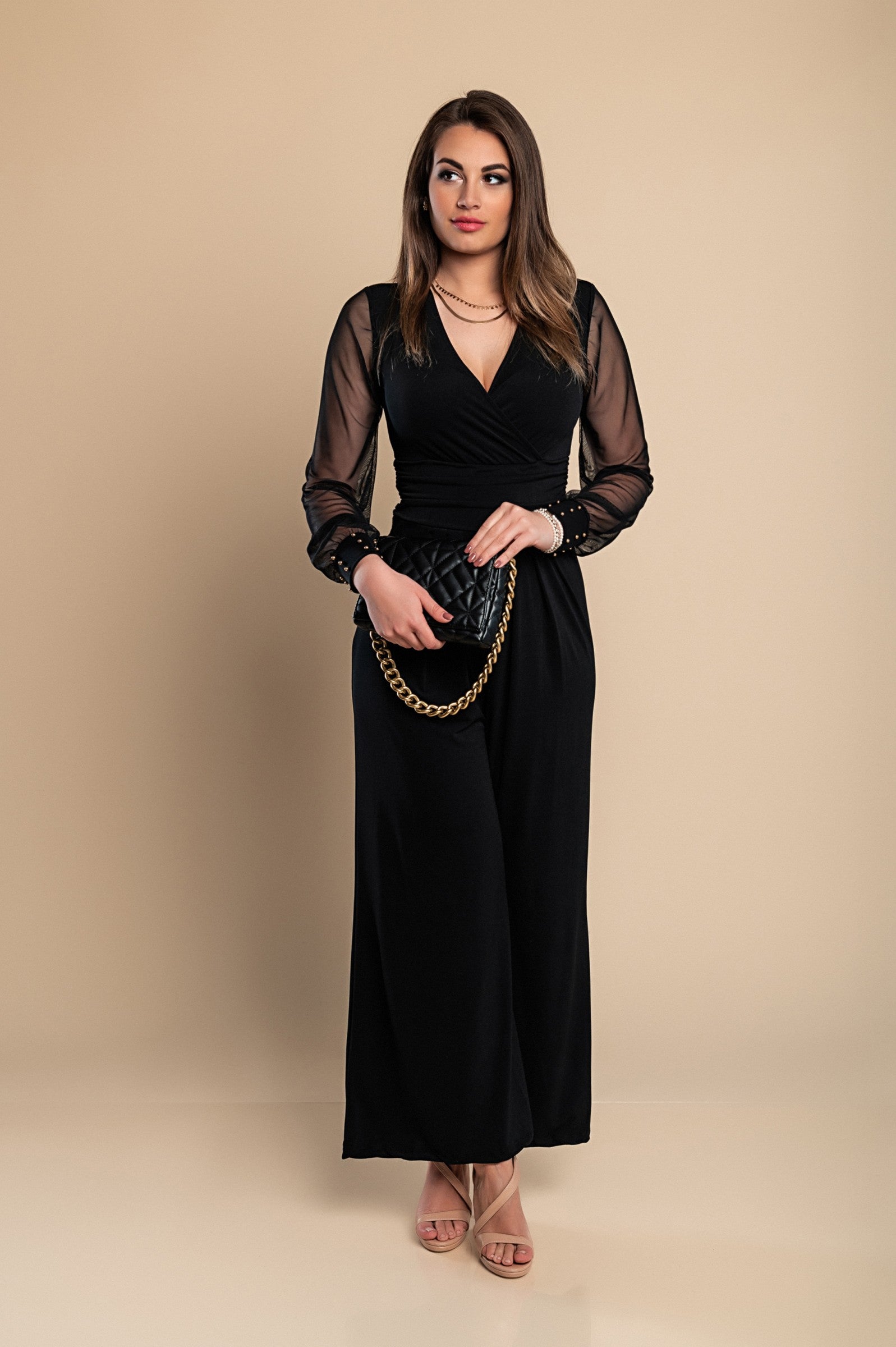 Elegant black jumpsuit with 'V' neckline and translucent long sleeves, featuring fashionable wrist accessories.