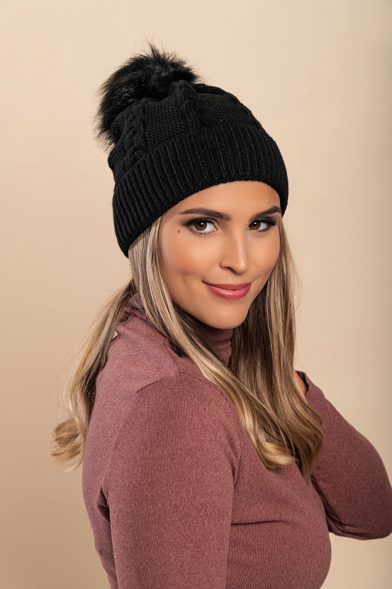 Black knitted hat with a faux fur pompom, featuring a rolled edge design, made from soft acrylic fabric.