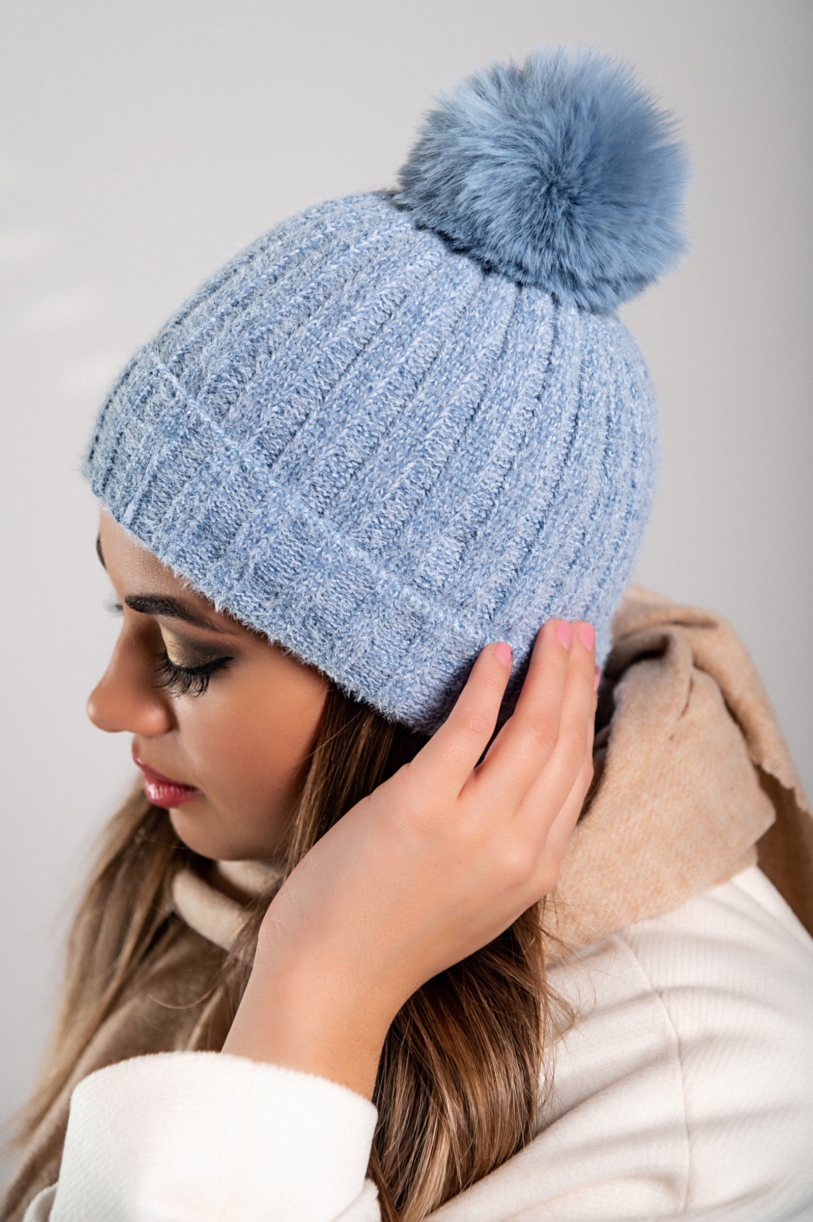 A stylish blue knitted hat with a faux fur pompom on top, featuring a folded hem and ribbed knit design.