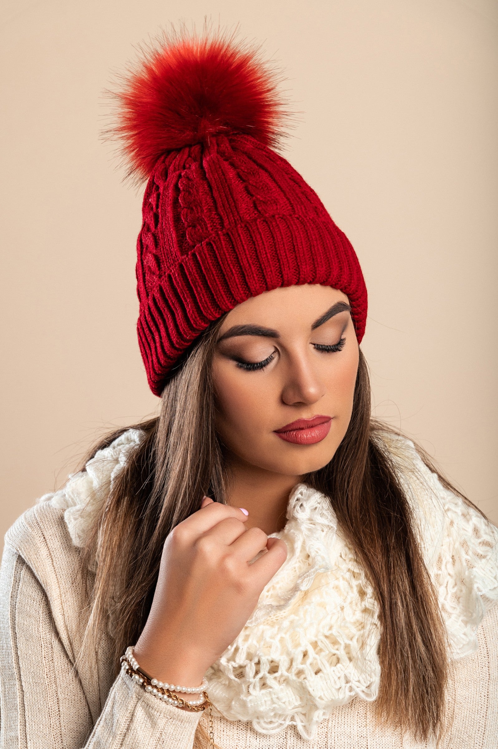 Burgundy knitted hat with a faux fur pompom on top, featuring a rolled edge design.