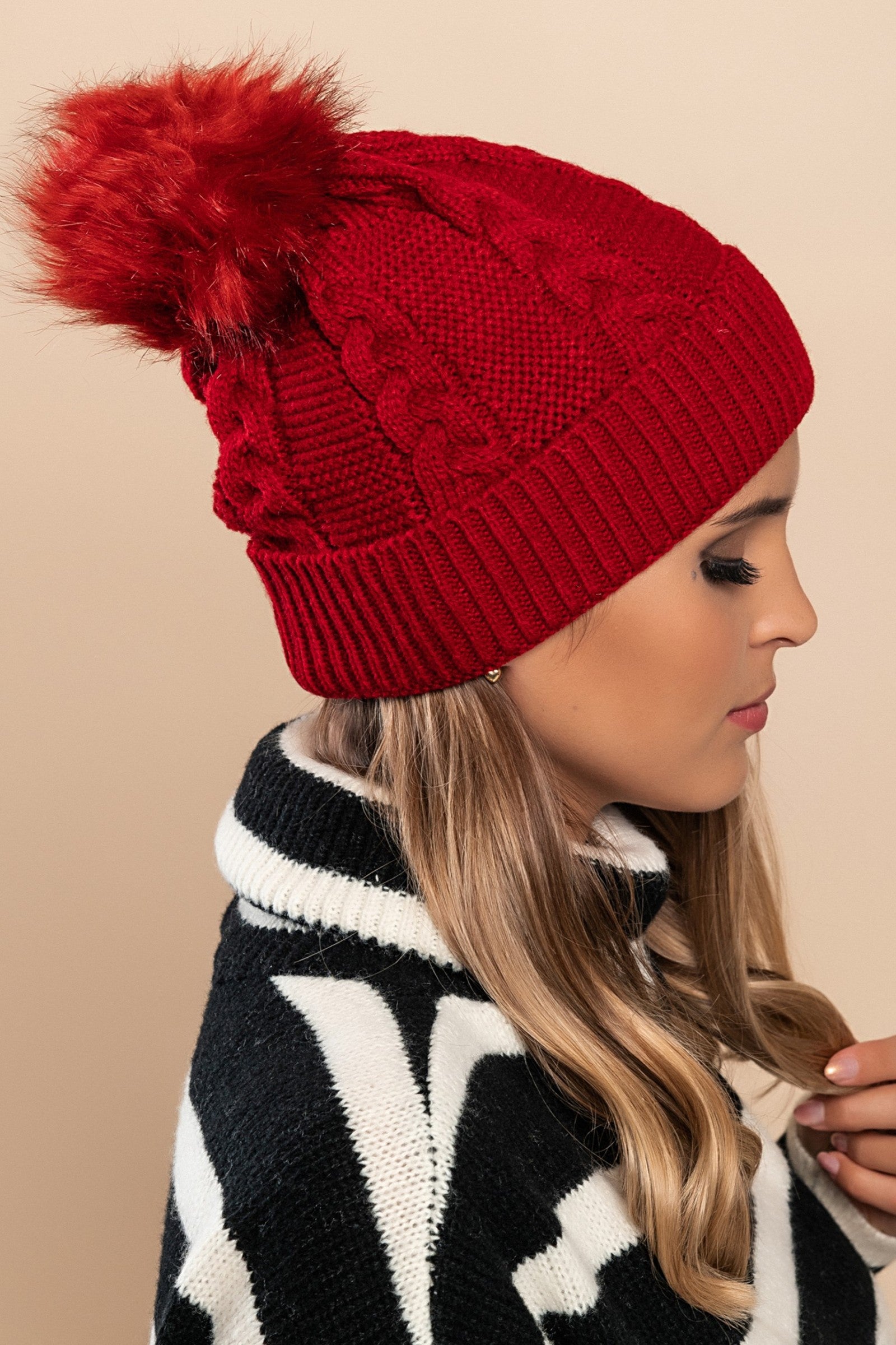 Burgundy knitted hat with a faux fur pompom on top, featuring a rolled edge design.