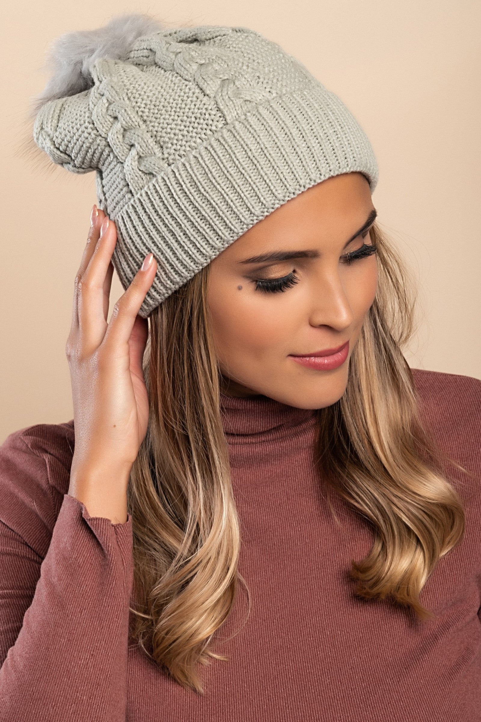 Light gray knitted hat with a faux fur pompom on top, featuring a rolled edge design.