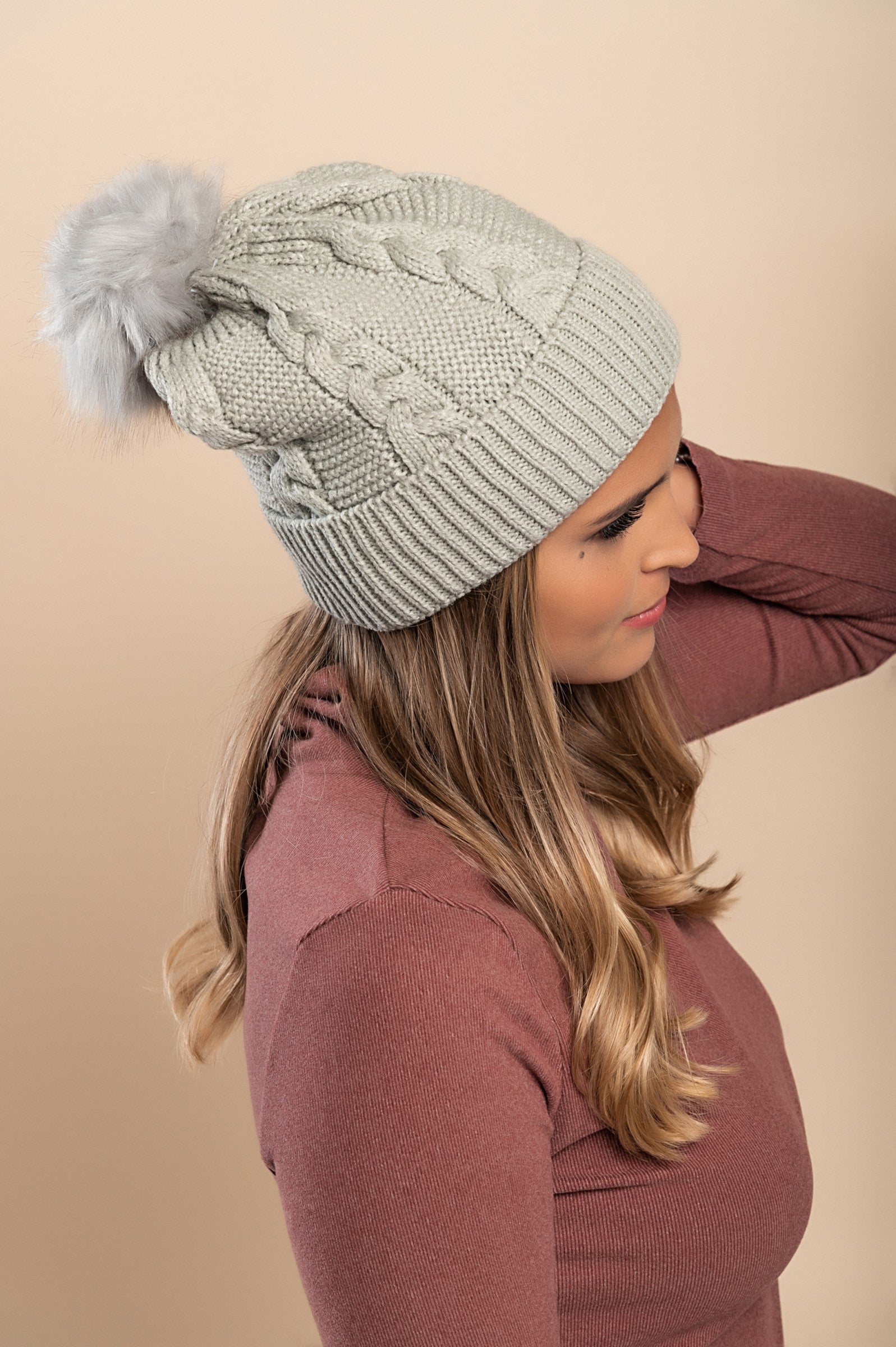 Light gray knitted hat with a faux fur pompom on top, featuring a rolled edge and ribbed knit design.