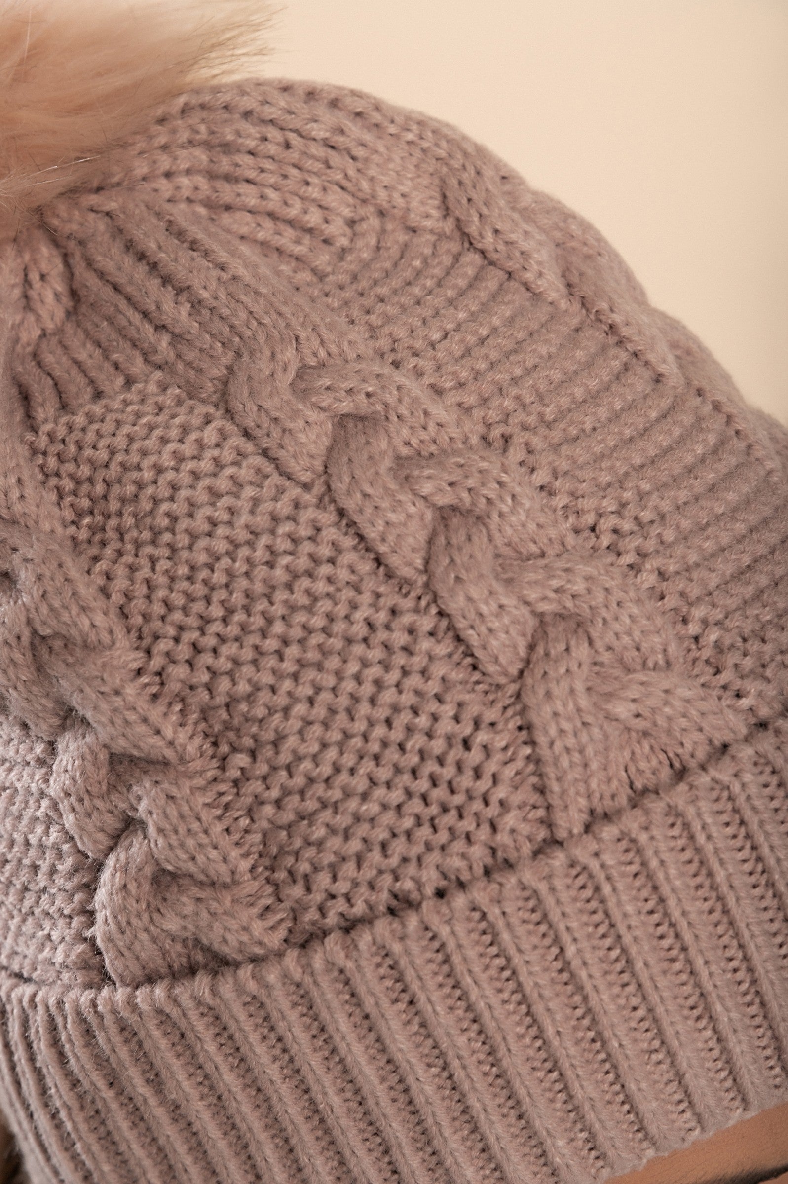 Light pink knitted hat with a faux fur pompom on top, featuring a rolled edge design.