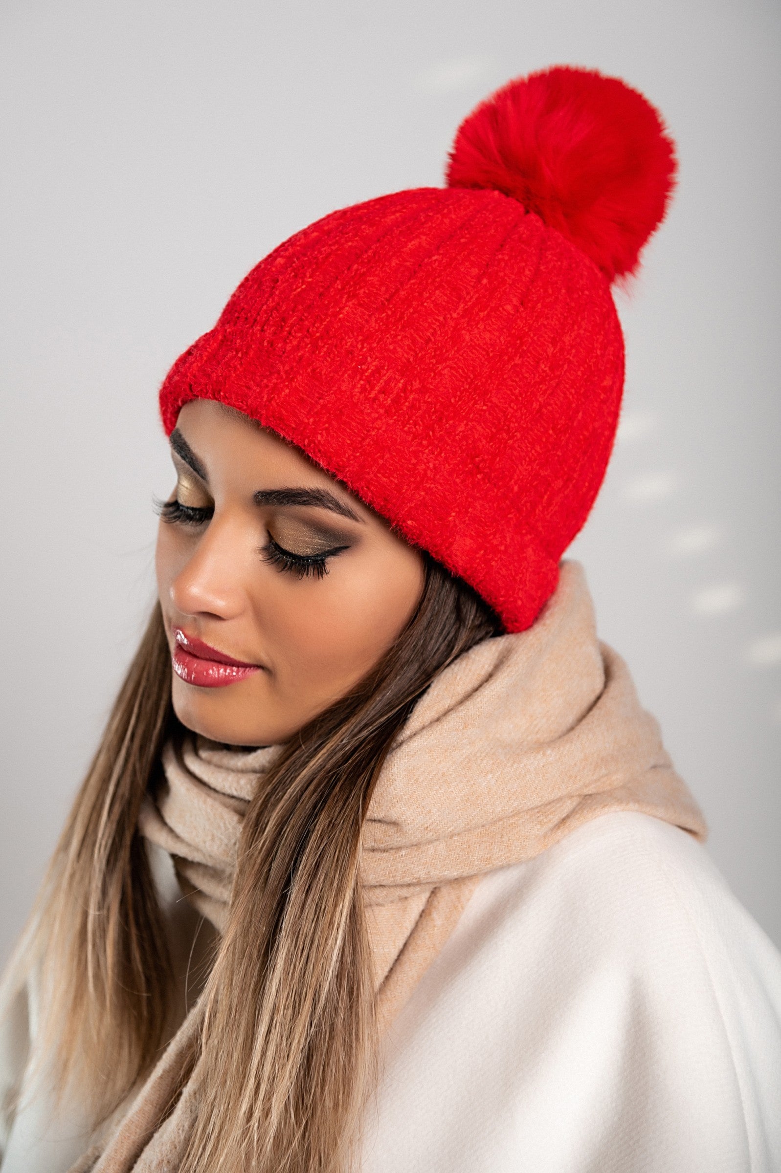 A vibrant red knitted hat with a faux fur pompom on top, showcasing a ribbed knit design and a folded hem for added comfort.