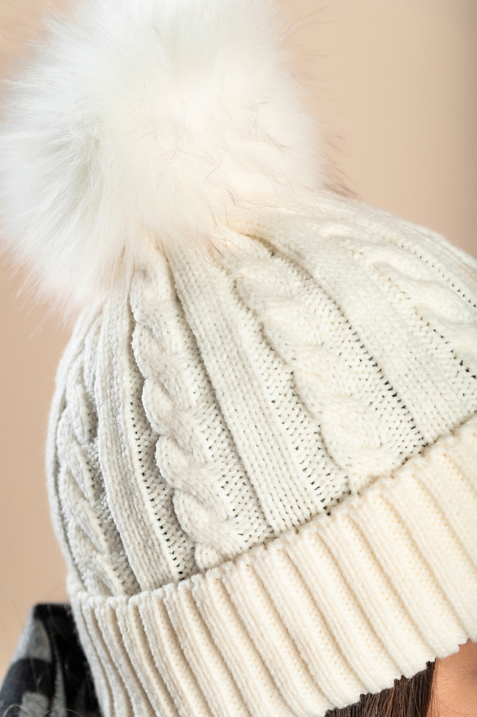 White knitted hat with a faux fur pompom on top, featuring a rolled edge design.