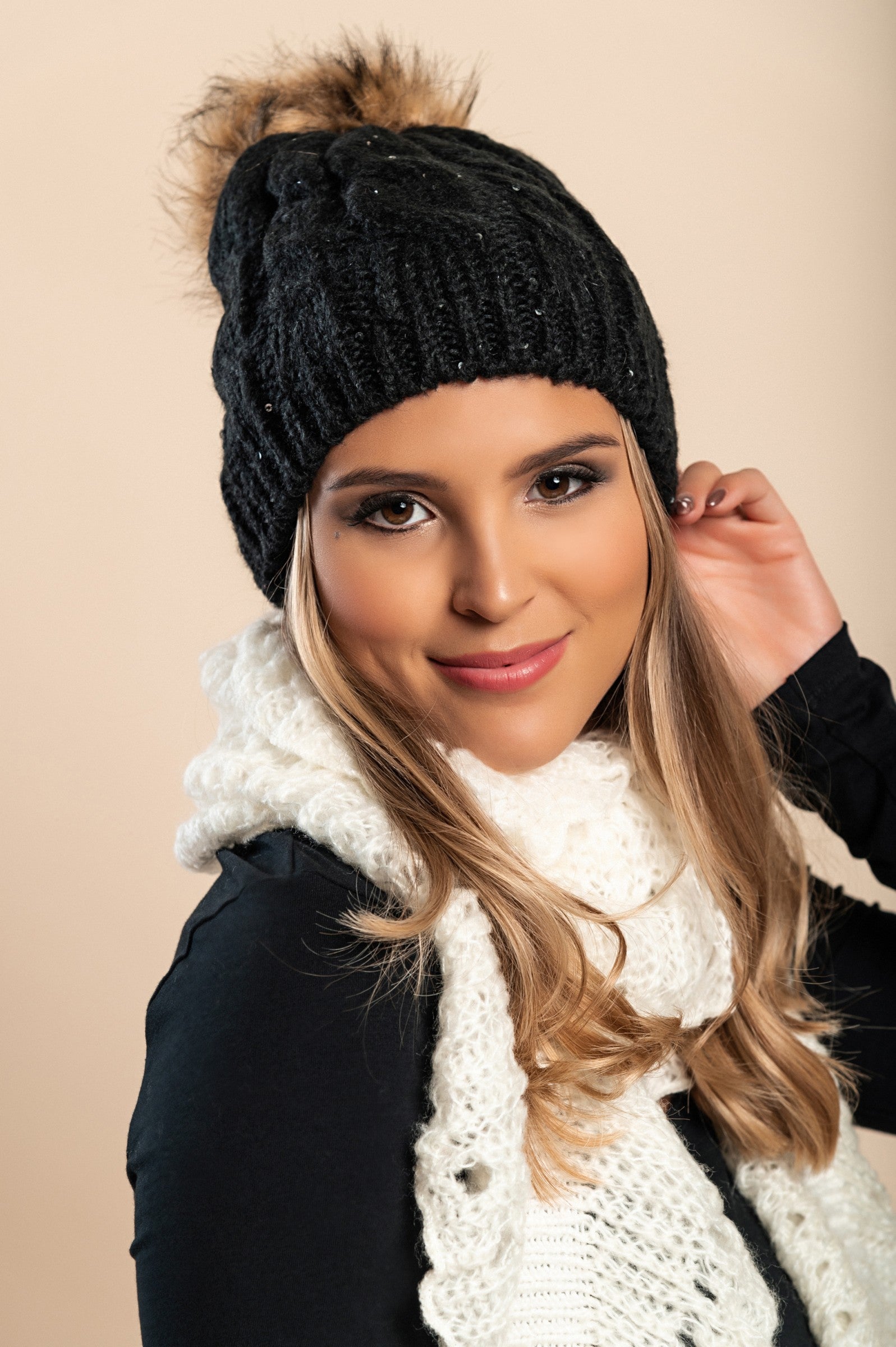 Black knitted hat with sequins and faux fur pompom, showcasing a rolled edge and ribbed knit design.