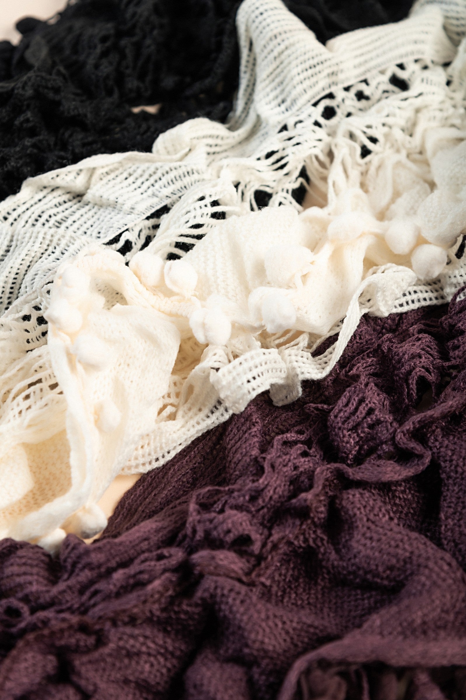 A vibrant set of three knitted scarves in black, white, and purple, showcasing their soft texture and stylish design.